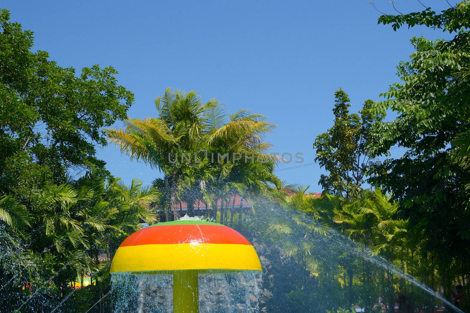 pool fountain with umbrella structure against trees and blue sky. 