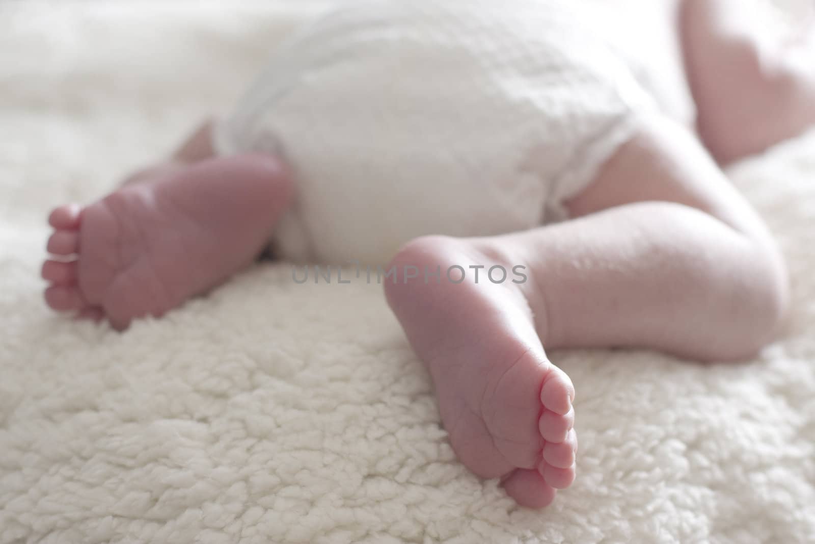 Less than one month old baby feet on a white fuzzy blanket