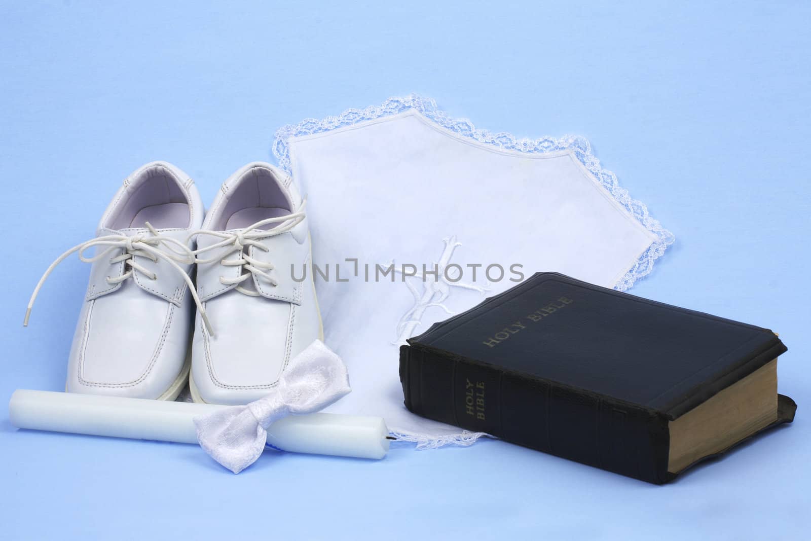 Religious baptism items, candle, shoes, bow tie, and bible on blue background