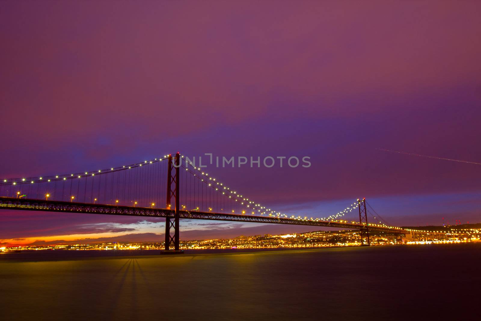 The 25 de Abril Bridge - suspension bridge over the river Tagus illuminated at night. Lisbon Portugal