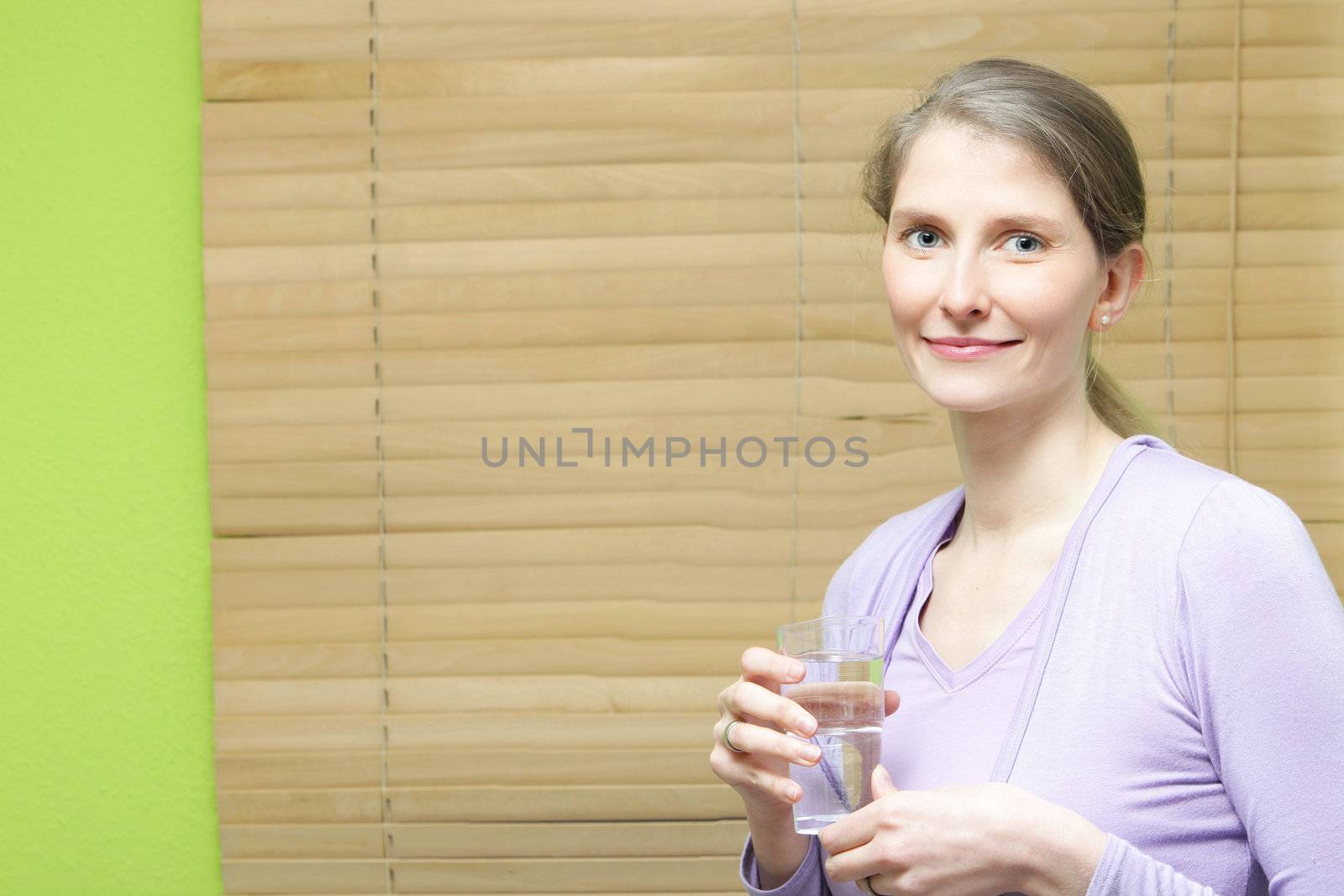 A young attractive woman holding a glass of water against wooden blinds.
