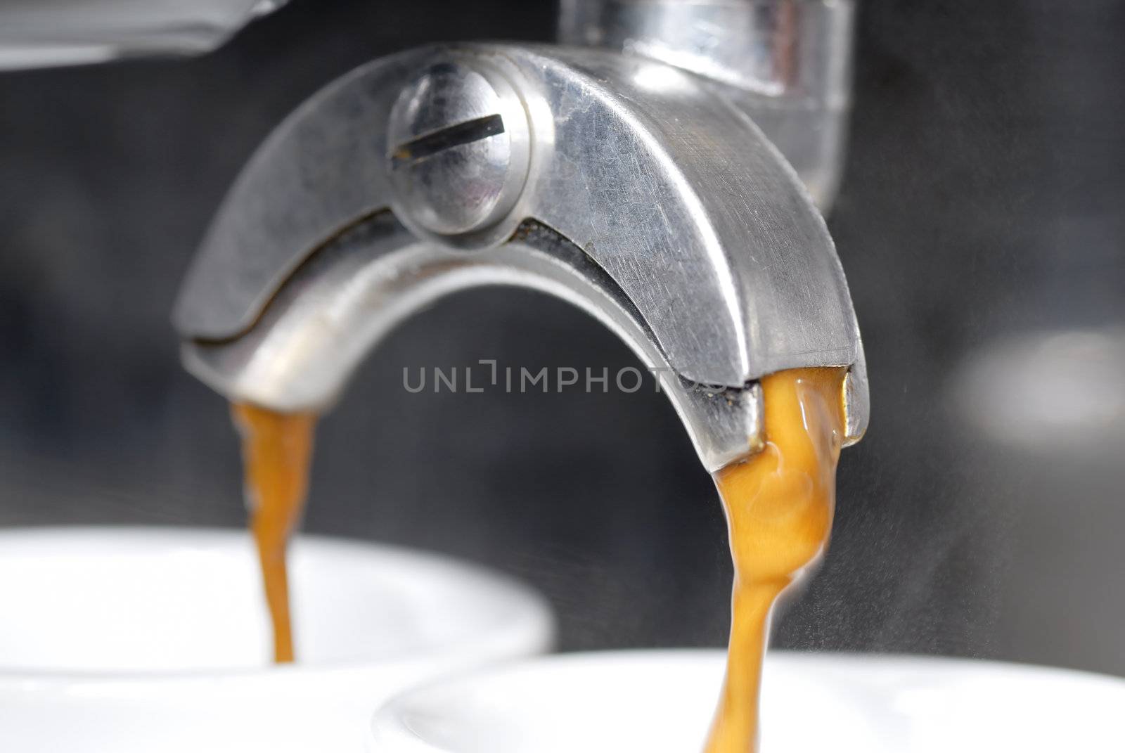 A shot of coffee pouring into two espresso cups. Focus on near portafilter spout.