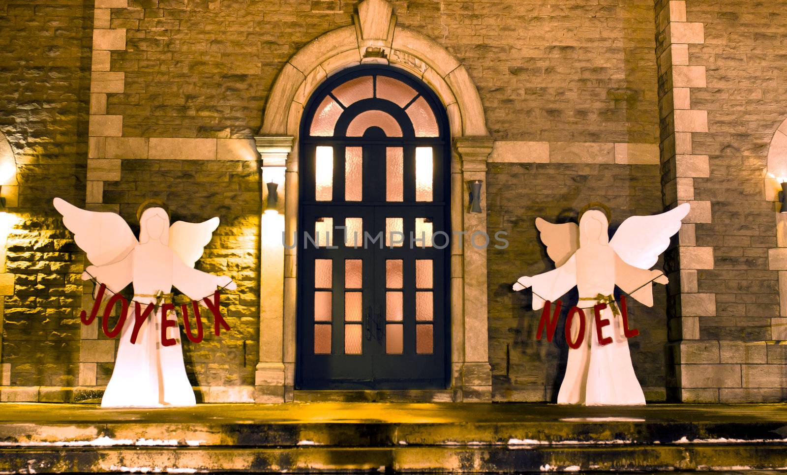 Church entrance decorated for Christmas with angels holding Joyeux Noel letters.