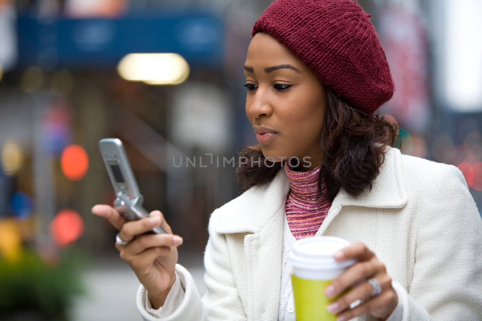 An attractive African American business woman checks her cell phone in the city.  She could be text messaging or even browsing the web via wi-fi or 4G connection.