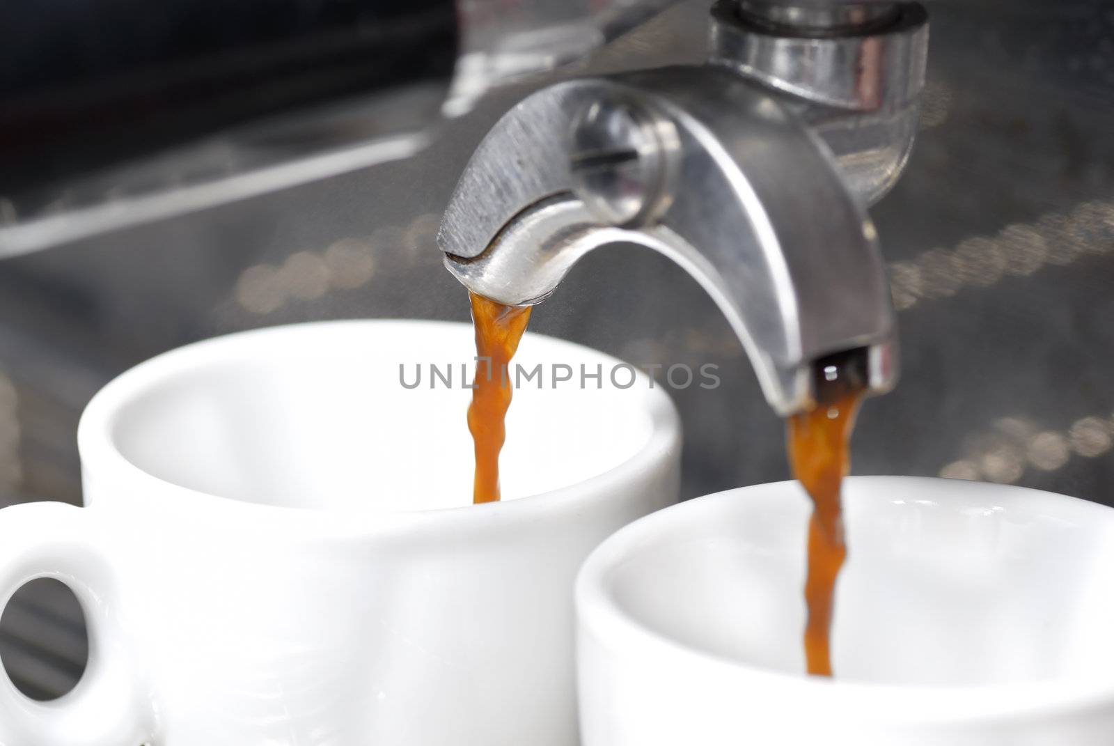 A shot of coffee pouring into two espresso cups. Focus on rear portafilter spout.