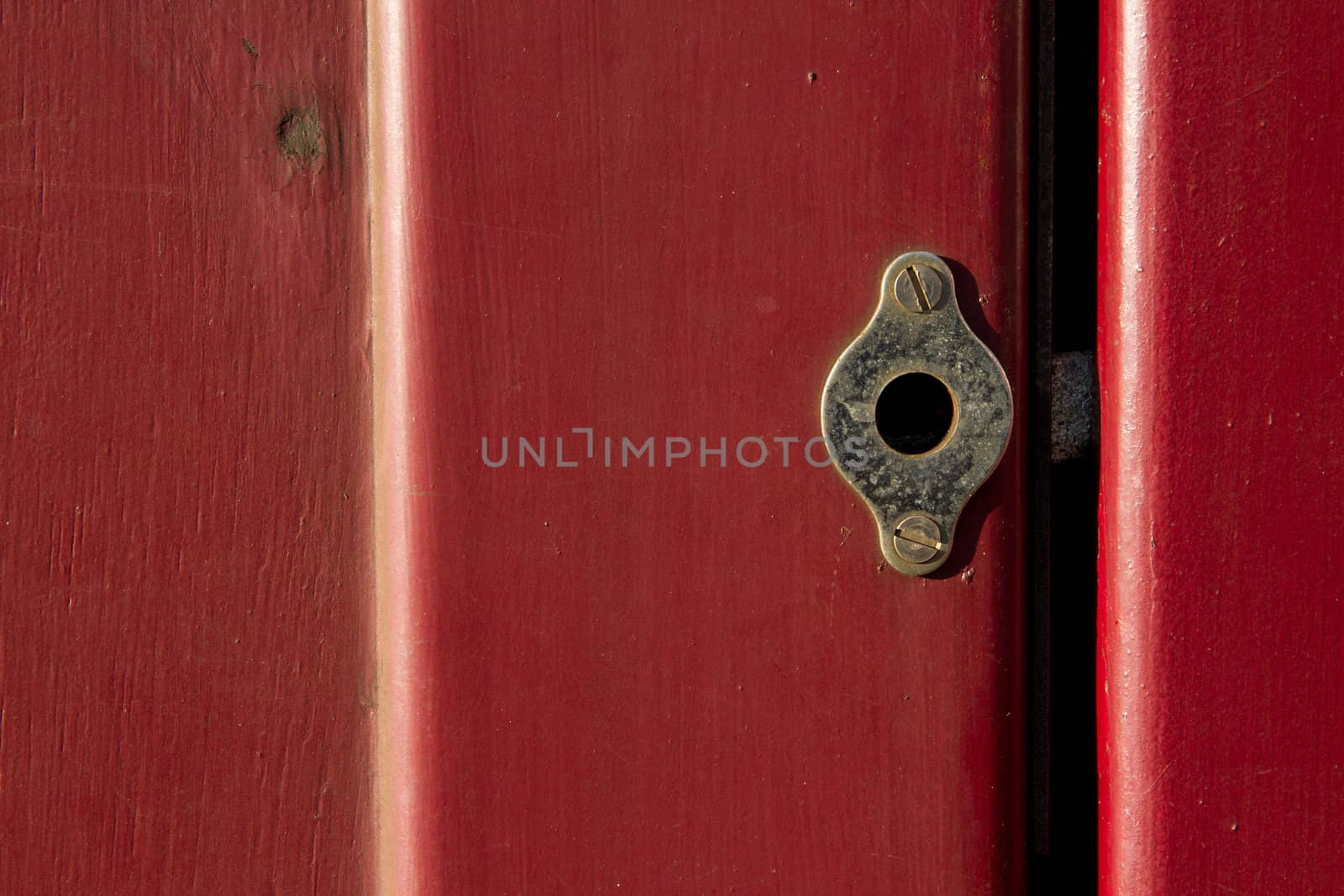 A vintage brass dead lock screwed to a red gloss painted door with the bolt showing in the gap.