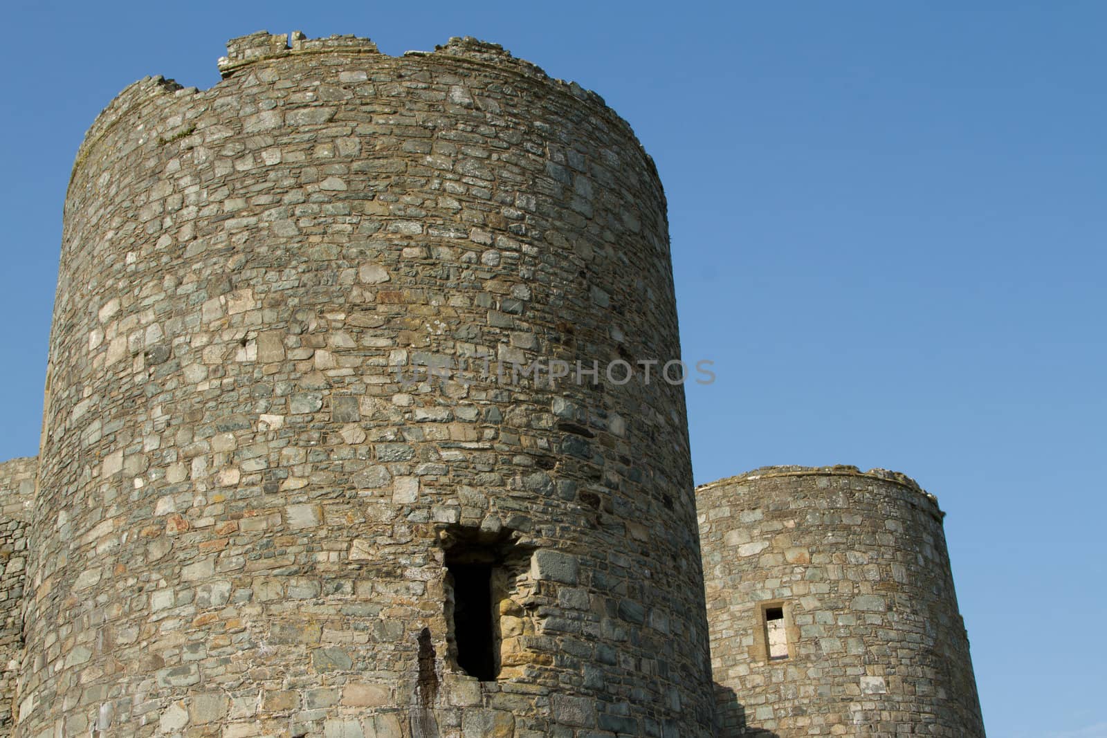 A pair of round castle towers made from stone with window openings set against a blue sky.