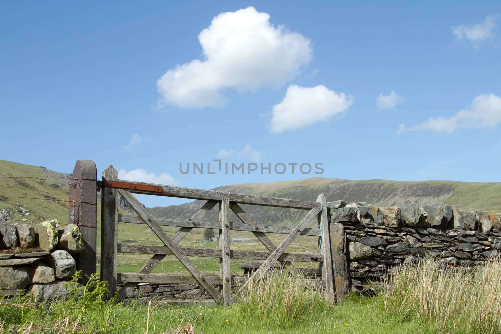 A rustic wooden gate on upland farmland with a stone wall and mountains in the distance.