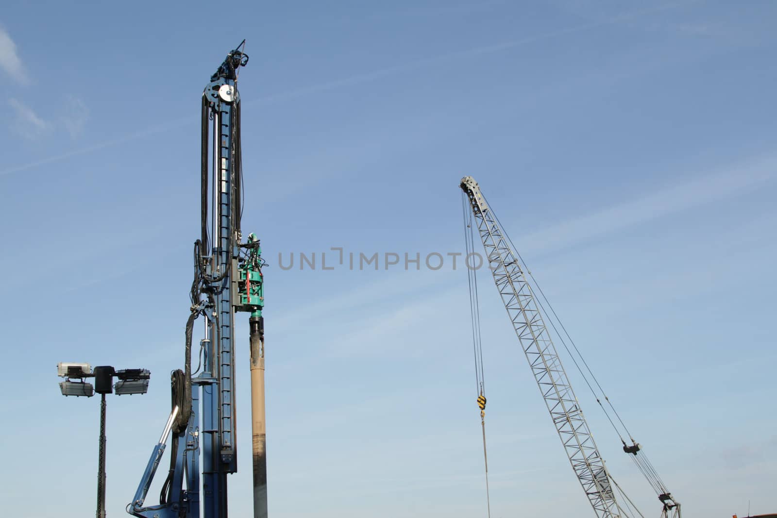 A blue painted pile driver and a crane set against a blue sky.