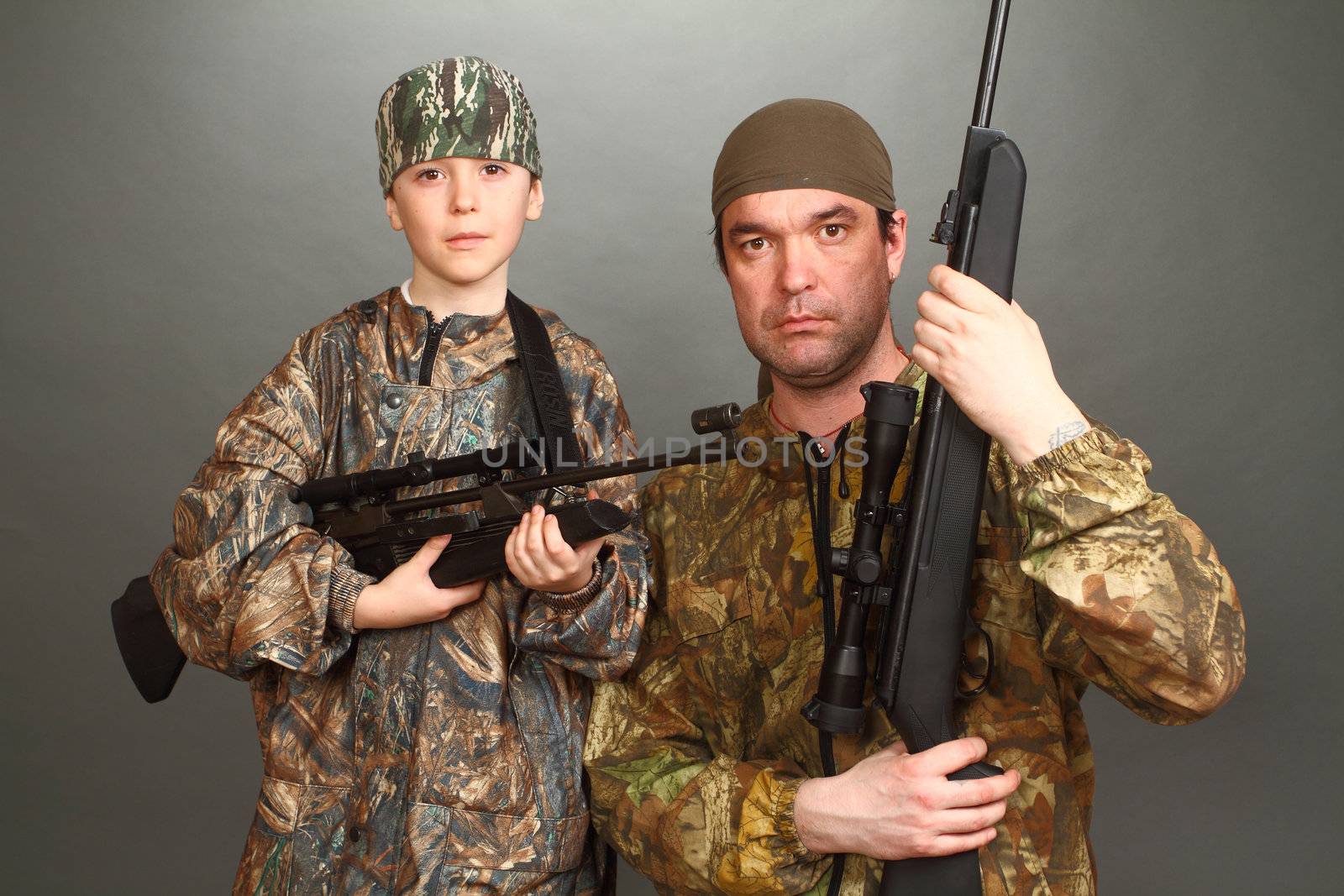 the boy and the adult man in a camouflage with rifles nearby in a shot, look in the chamber