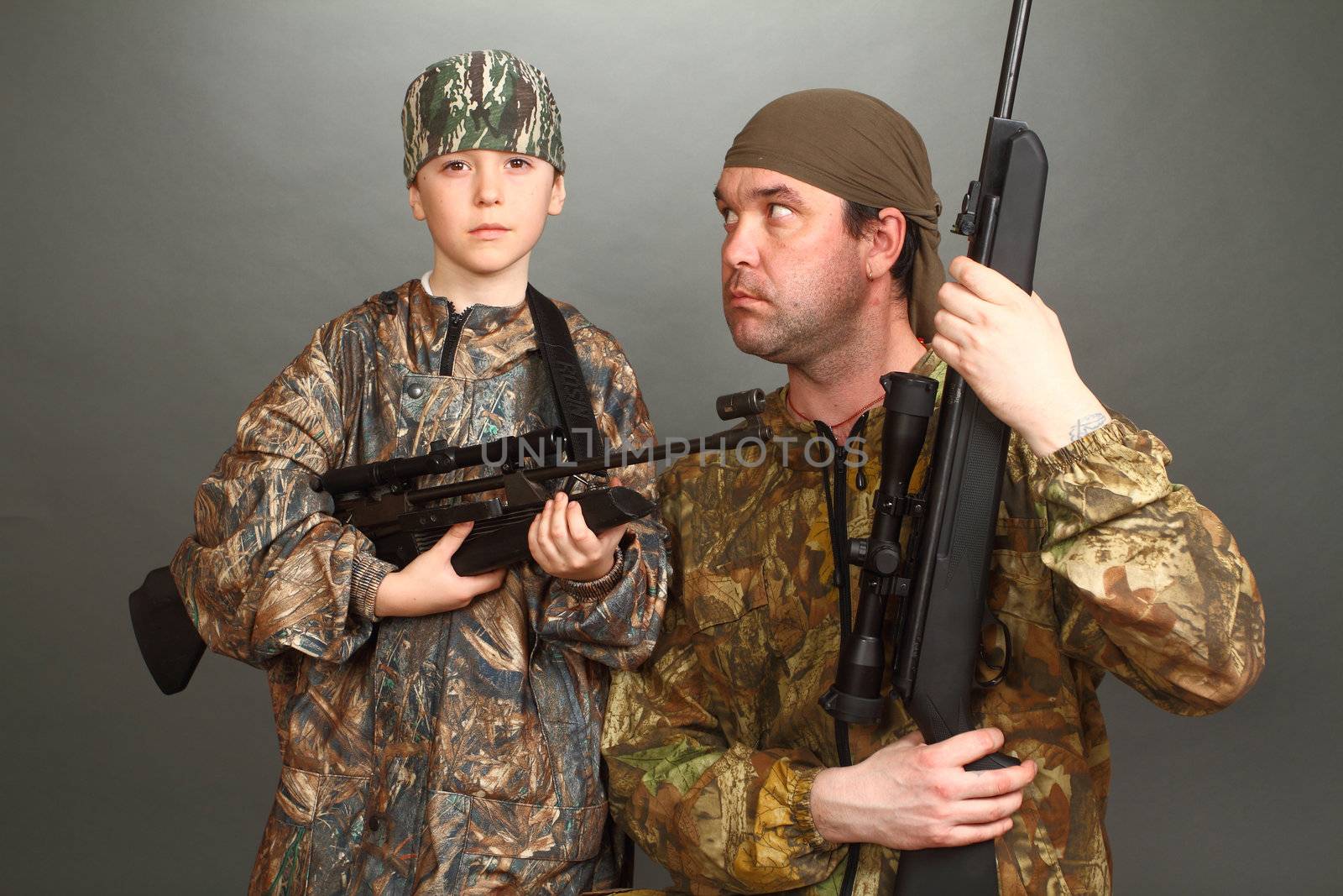 the boy and the adult man in a camouflage with rifles nearby in a shot