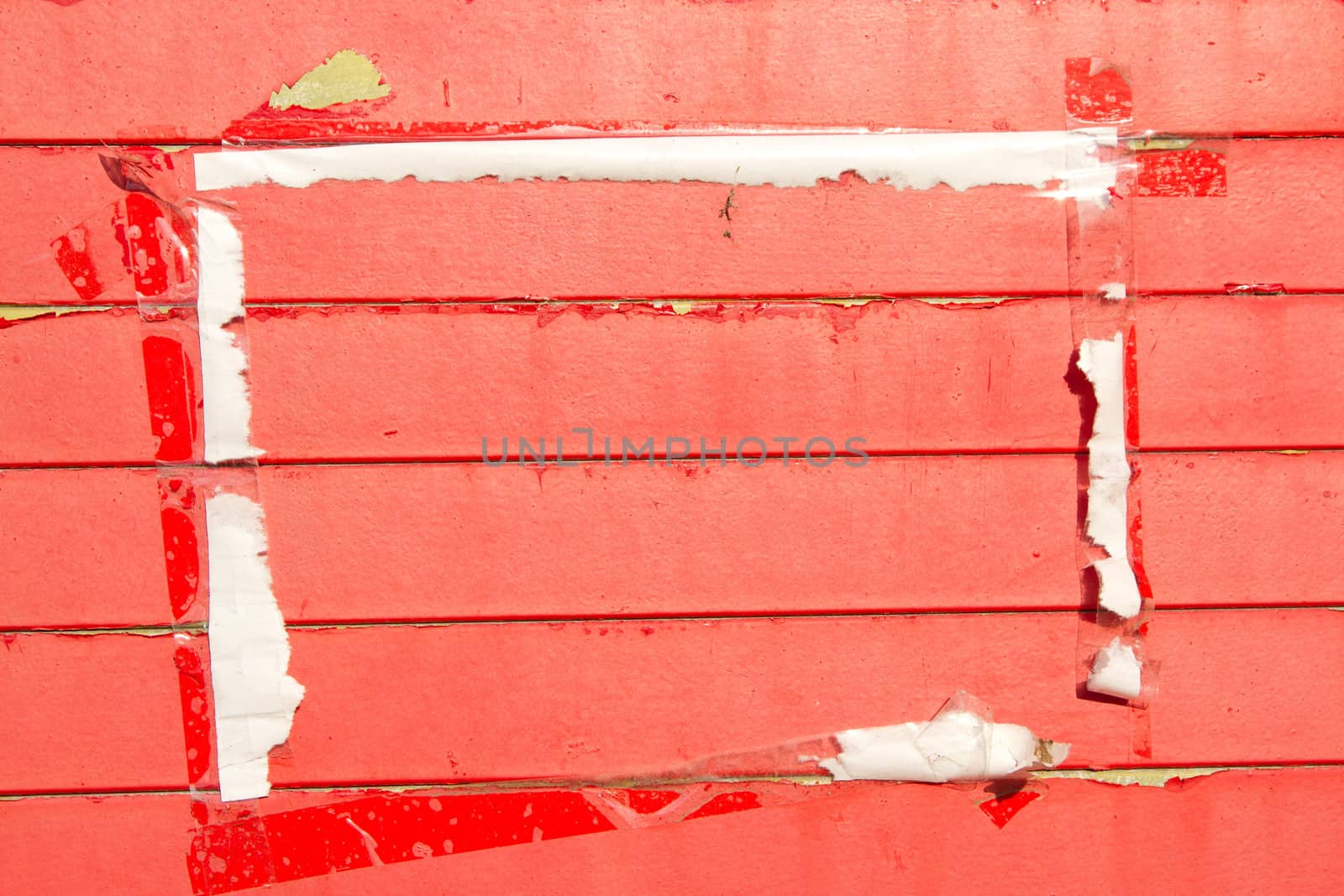 Wooden horizontal slats painted red with areas of flaking paint and a framed area with a paper and tape surround.