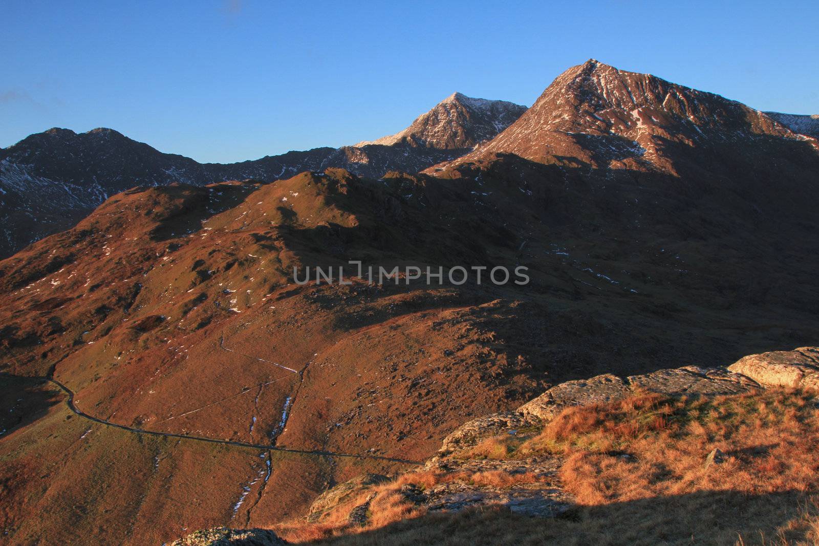 The East side of the Snowdon Massif in the dawn light with the miners track visible and the peaks of Crib Goch and Snowdon against a blue sky, Snowdonia National Park, Wales, UK.