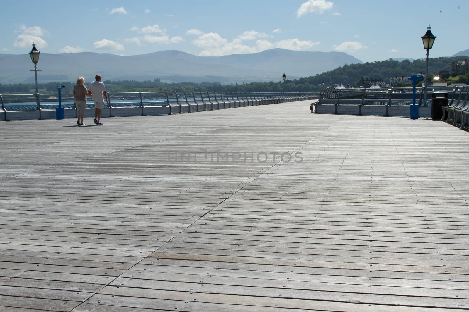 A couple walks arm in arm along the board walk of a pier.