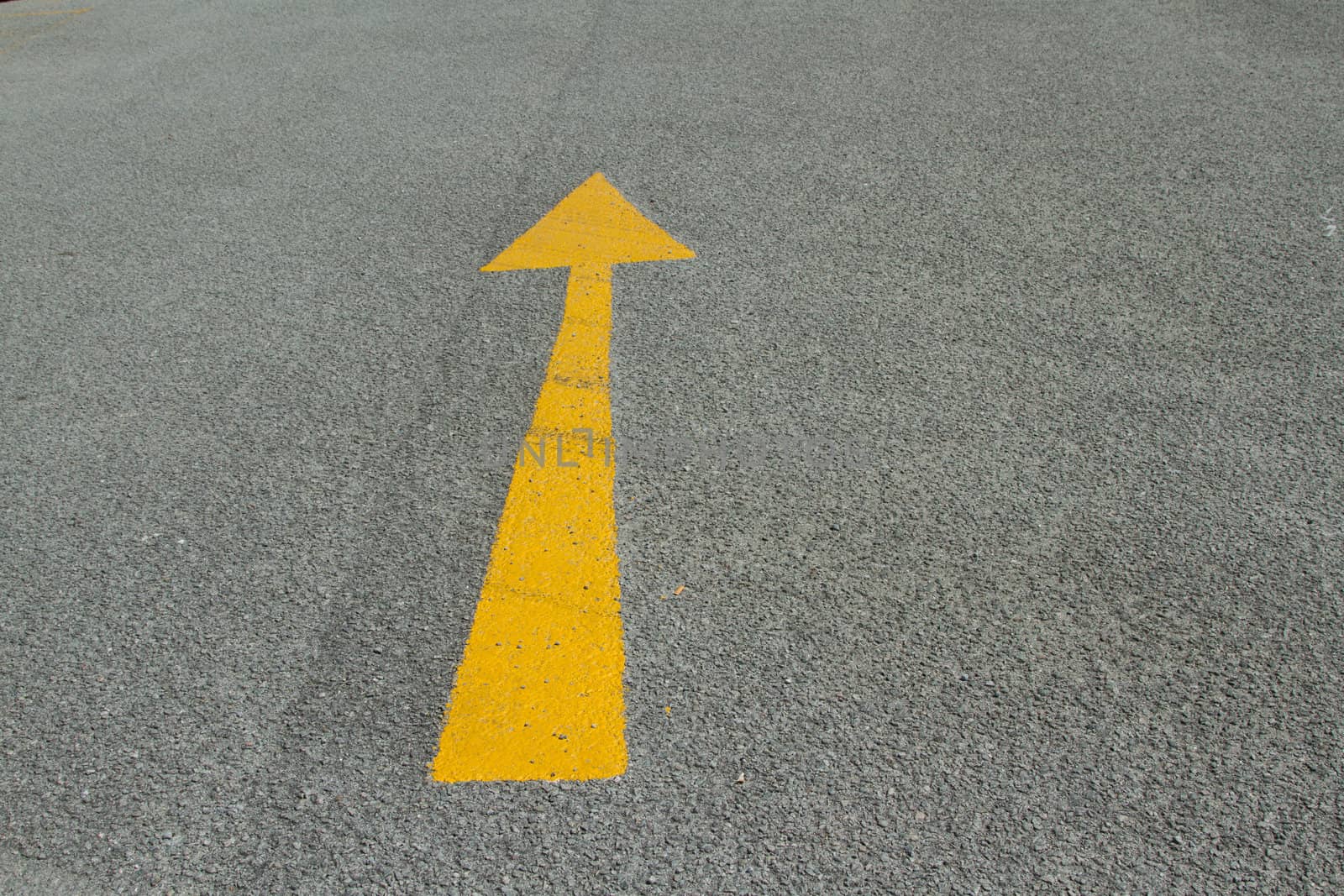 An area of grey tarmac with a yellow painted arrow pointing forward.