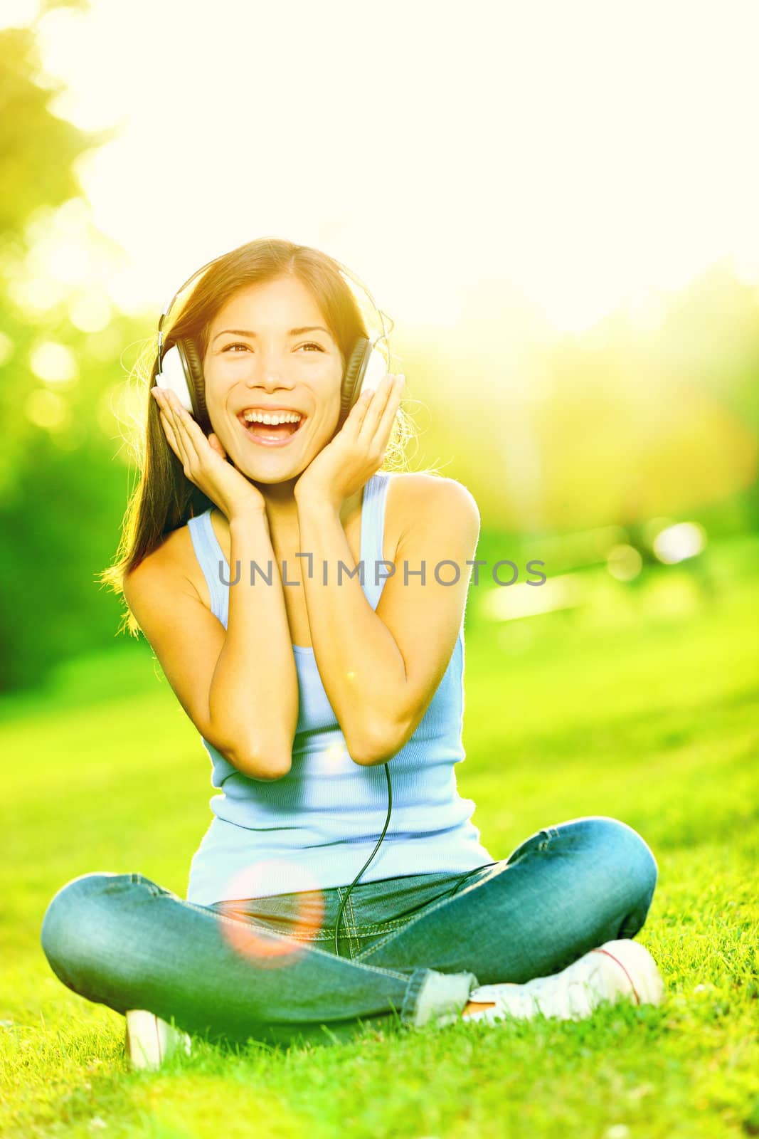 Music headphones woman in park singing listening to music on smart phone or mp3 player in sunshine in park. Mixed race Asian / Caucasian girl smiling happy.