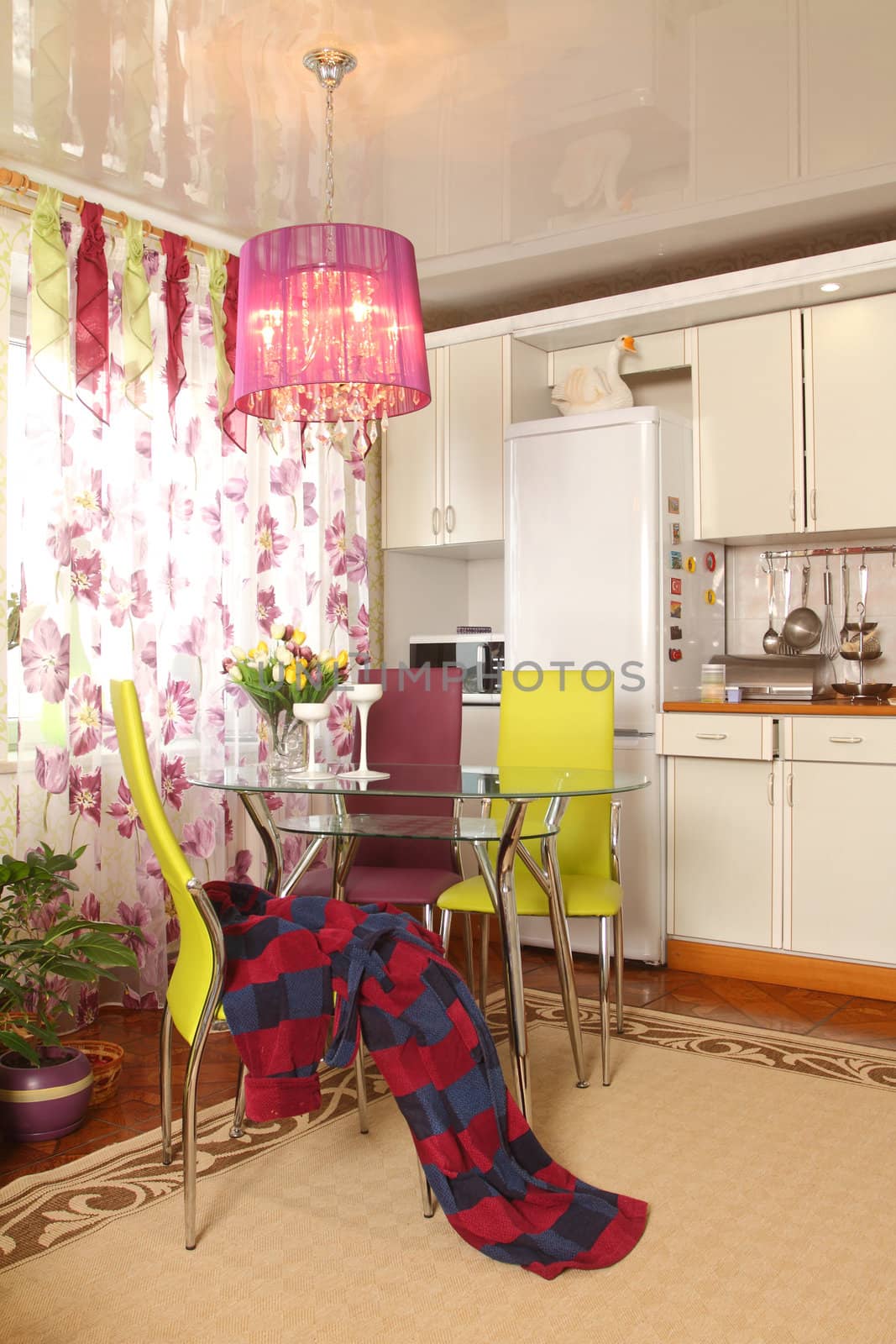 Modern kitchen. A bunch of flowers on a glass little table opposite to a window, the dressing gown thrown on a chair