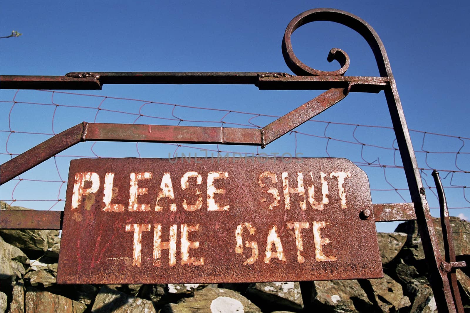 A metal rusty sign on an old gate  with the words 'PLEASE SHUT THE GATE'.