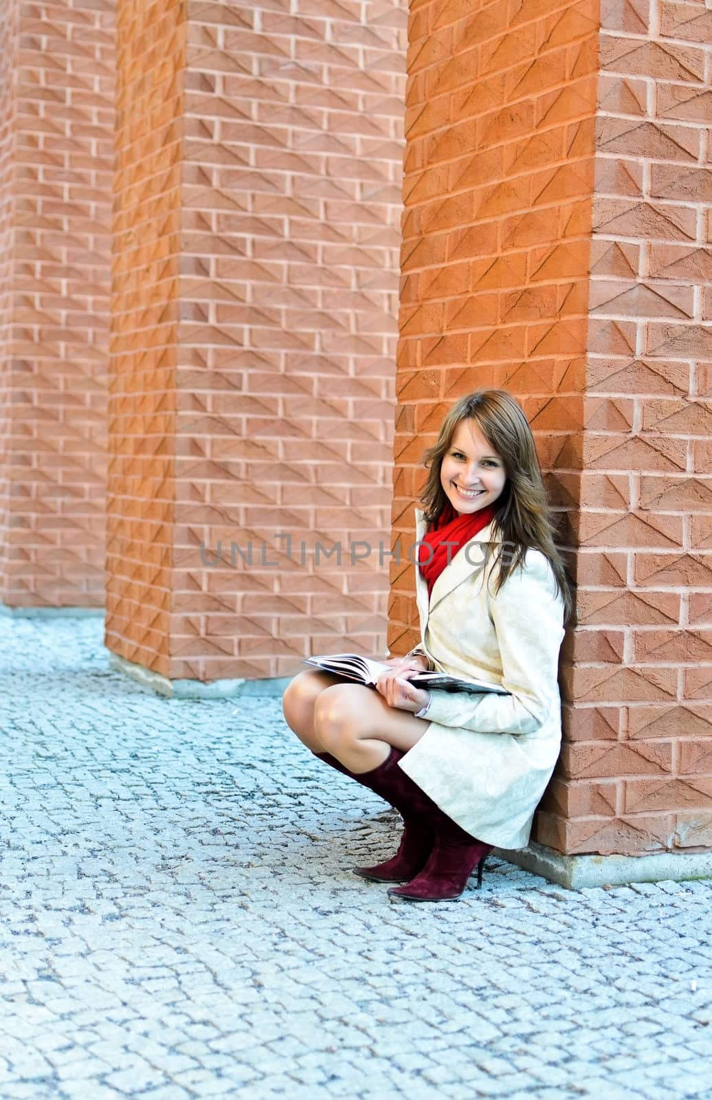 Smiling female sits and reads a book at the wall