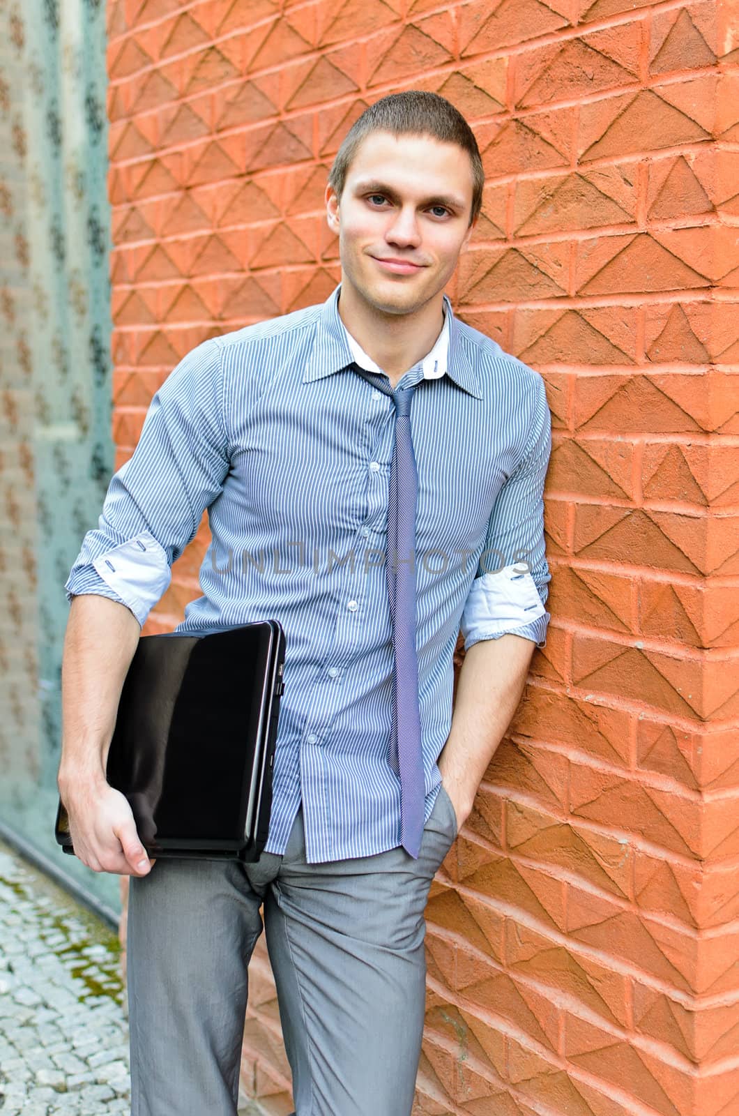 Portrait of a student with a laptop standing at the wall