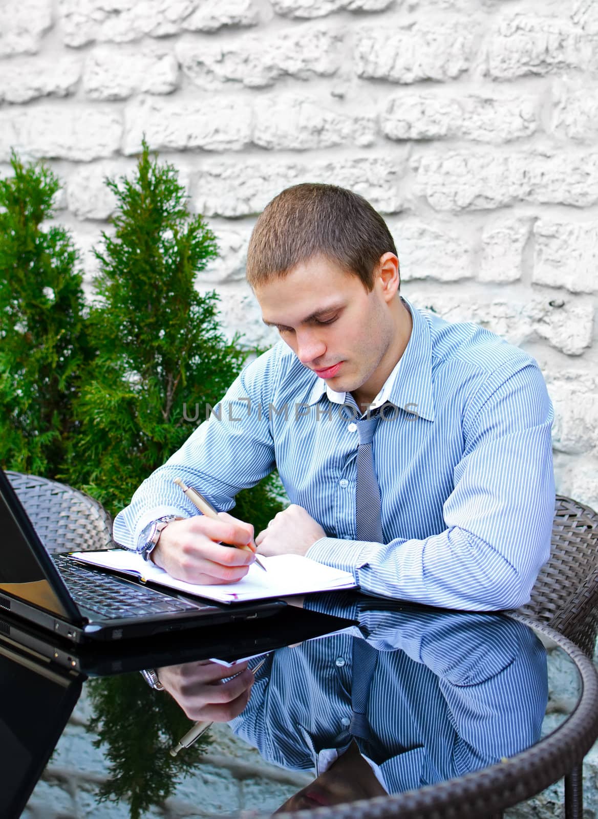 Businessman with laptop in cafe on the street. Makes notes with pen