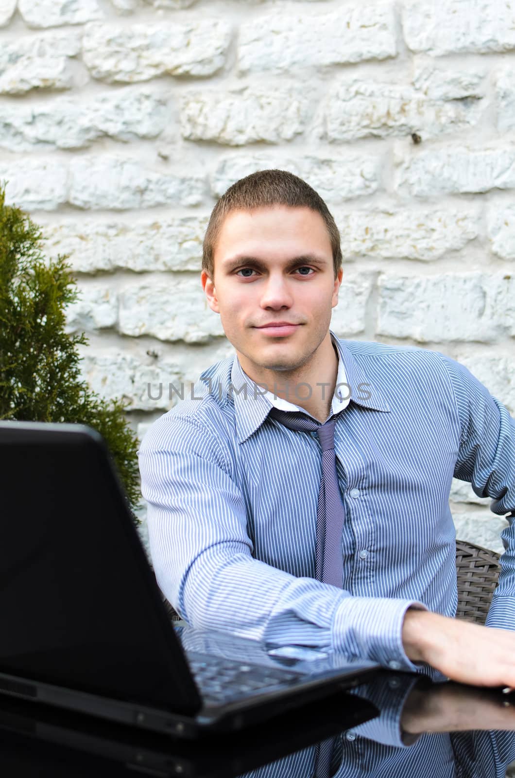 Businessman with laptop in cafe on the street. Makes notes with pen