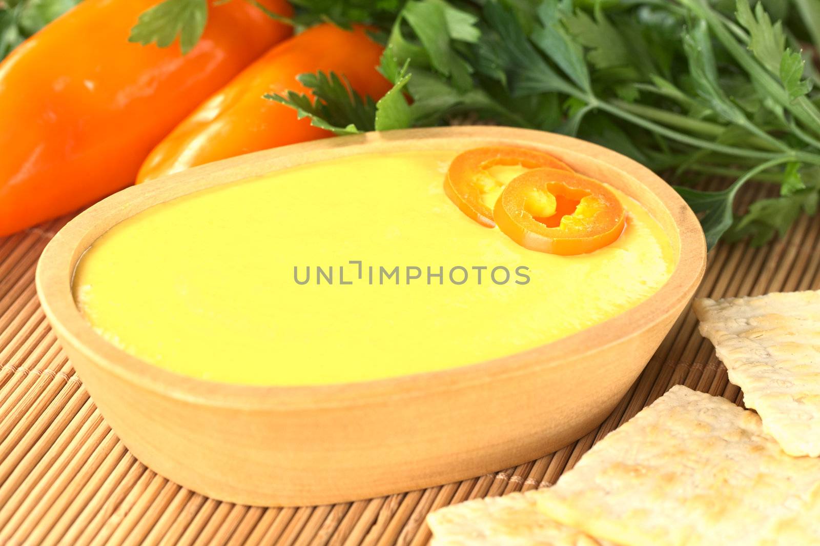 Peruvian Huancaina Sauce (spicy cheese sauce) made of cheese, soda crackers, aji (Peruvian yellow chili pepper) and milk in a wooden bowl (Selective Focus, Focus on the front of the aji slices on the sauce) 