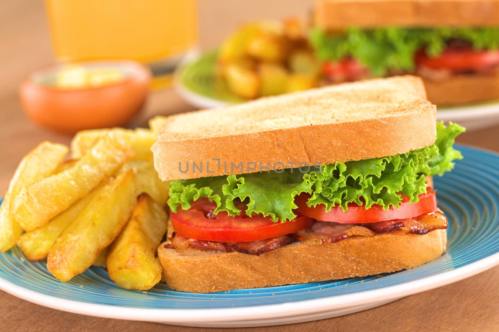 Fresh homemade BLT (bacon lettuce and tomato) sandwich with French fries on plate with juice in the back (Selective Focus, Focus on the front of the sandwich) 