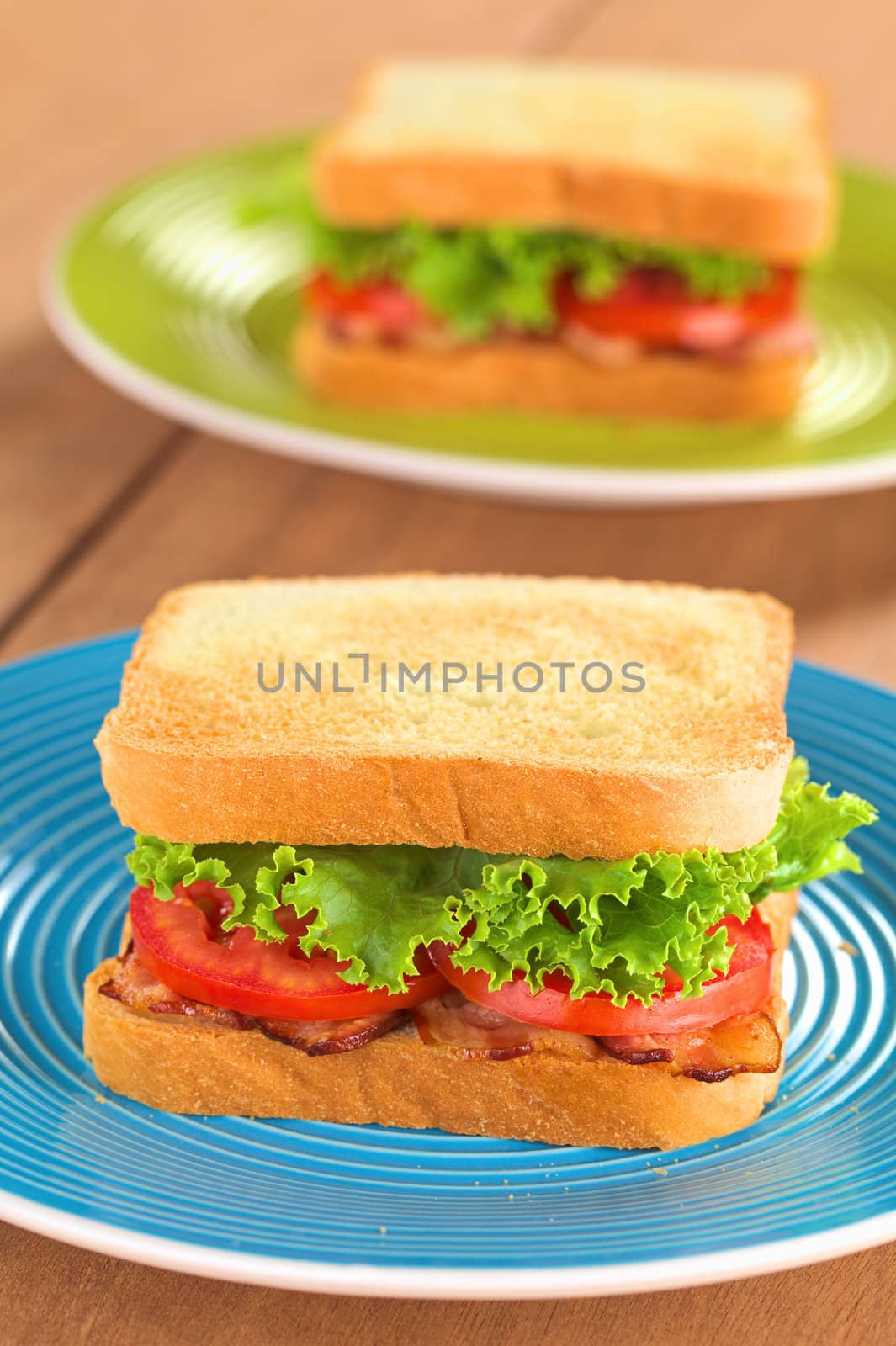 Fresh homemade BLT (bacon lettuce and tomato) sandwich on colorful plates (Selective Focus, Focus on the front of the first sandwich) 