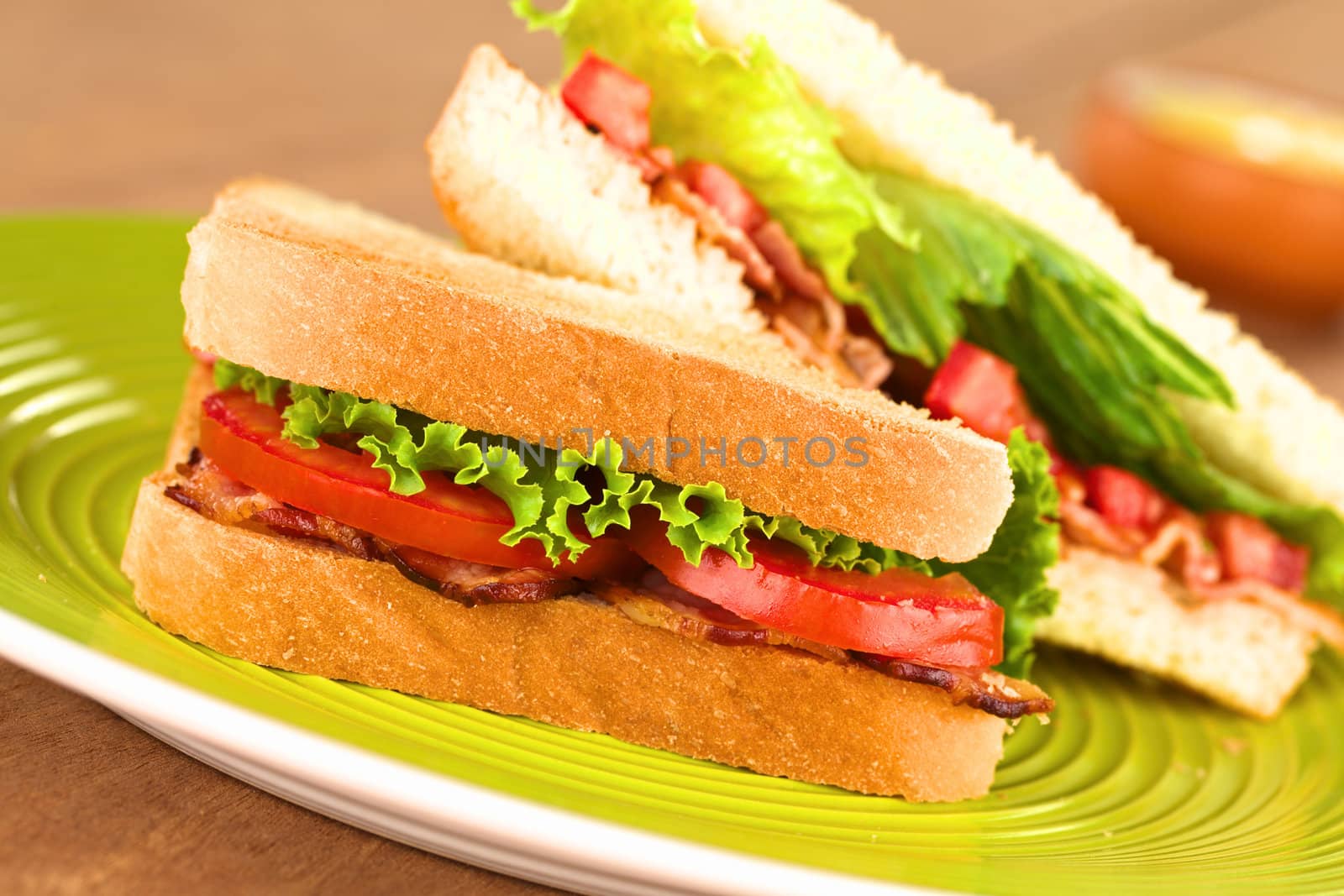 Fresh homemade BLT (bacon lettuce and tomato) sandwich halves on green plate with mayonnaise in the back (Selective Focus, Focus on the front of the sandwich) 