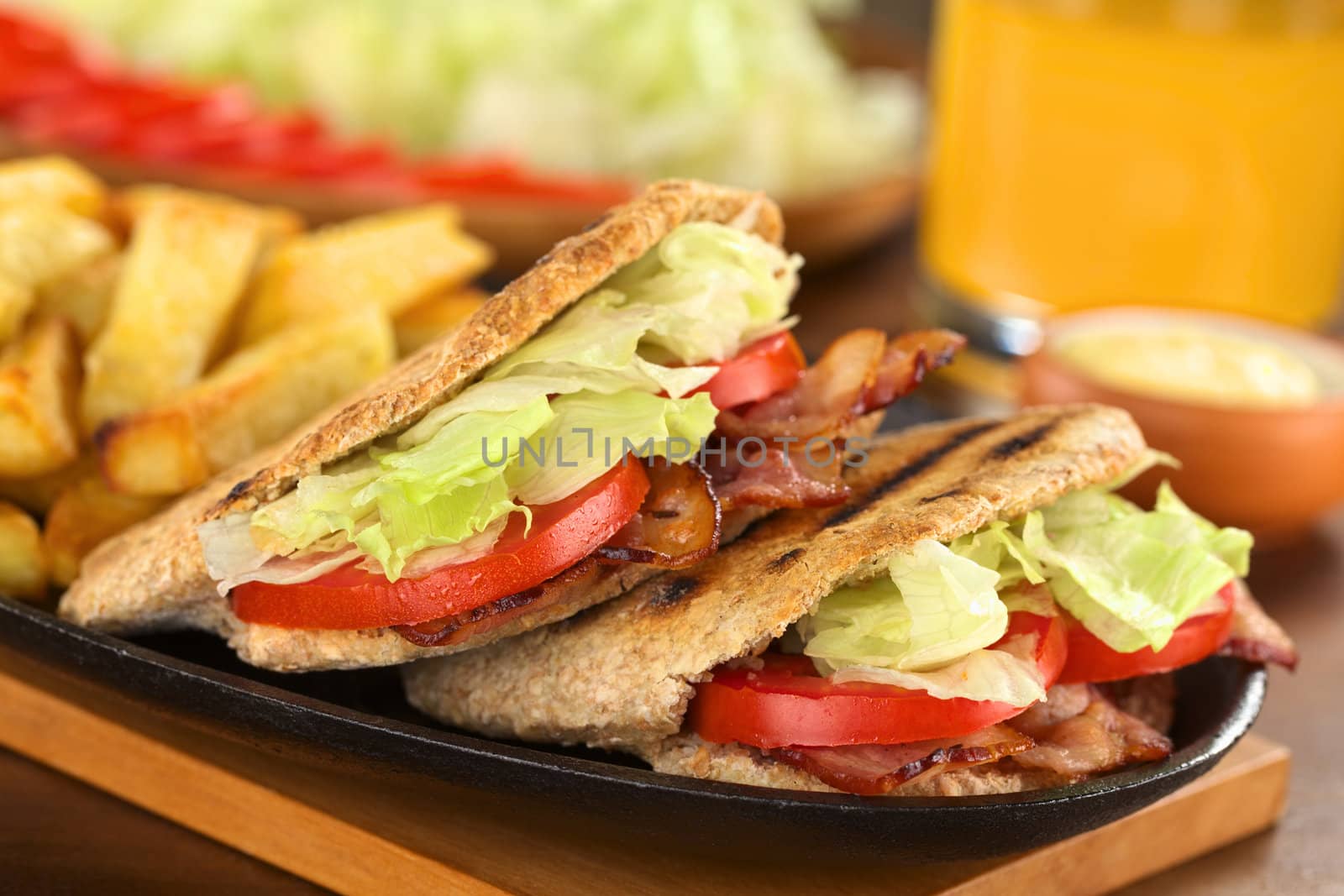 Fresh homemade BLT (bacon lettuce and tomato) wholewheat pita sandwich with French fries on metallic plate with mayonnaise and juice (Selective Focus, Focus on the front of the two pita stuffings) 