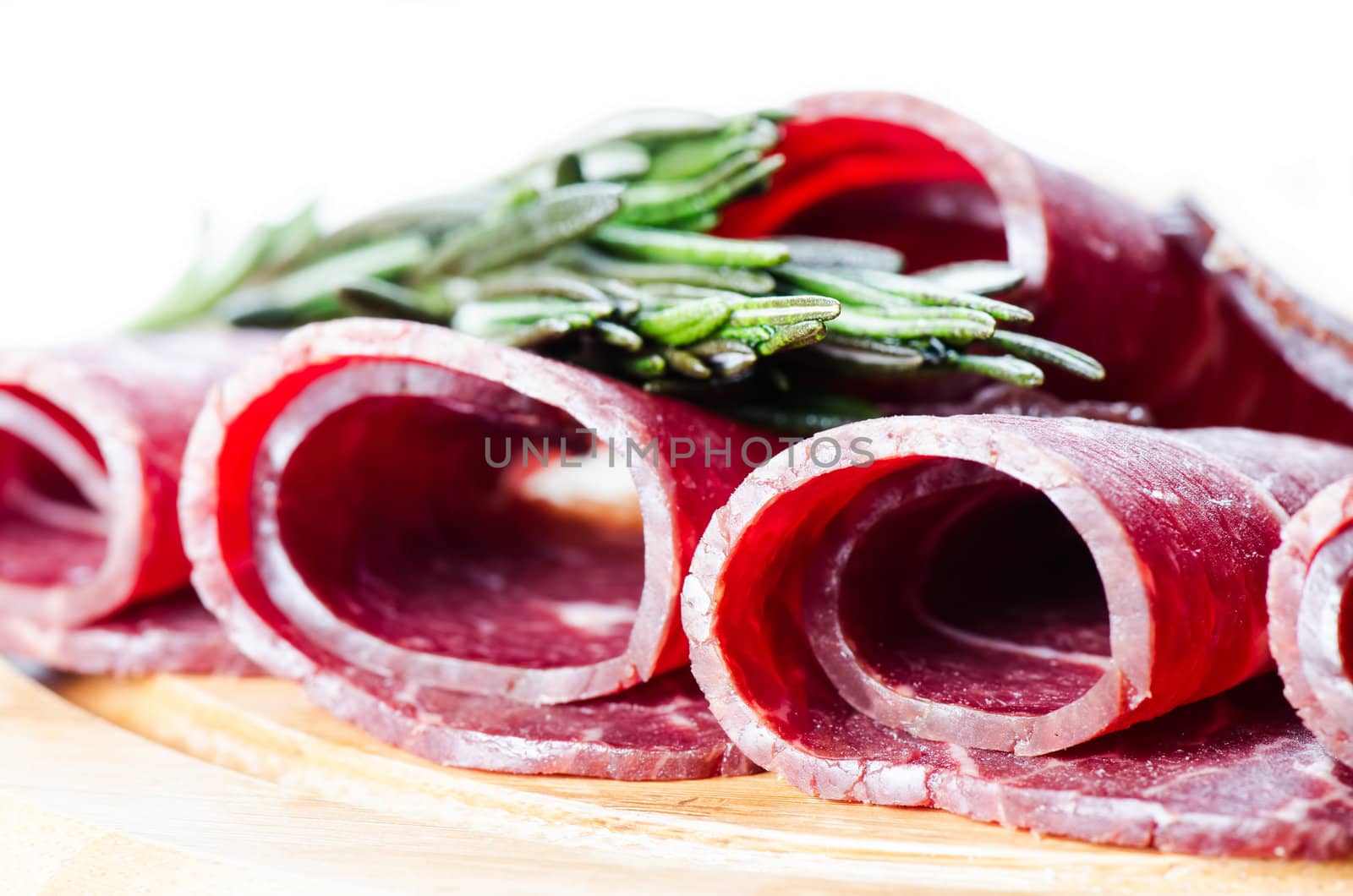 Rolls of cured smoked beef on wooden board with rosmary on wooden cutting board