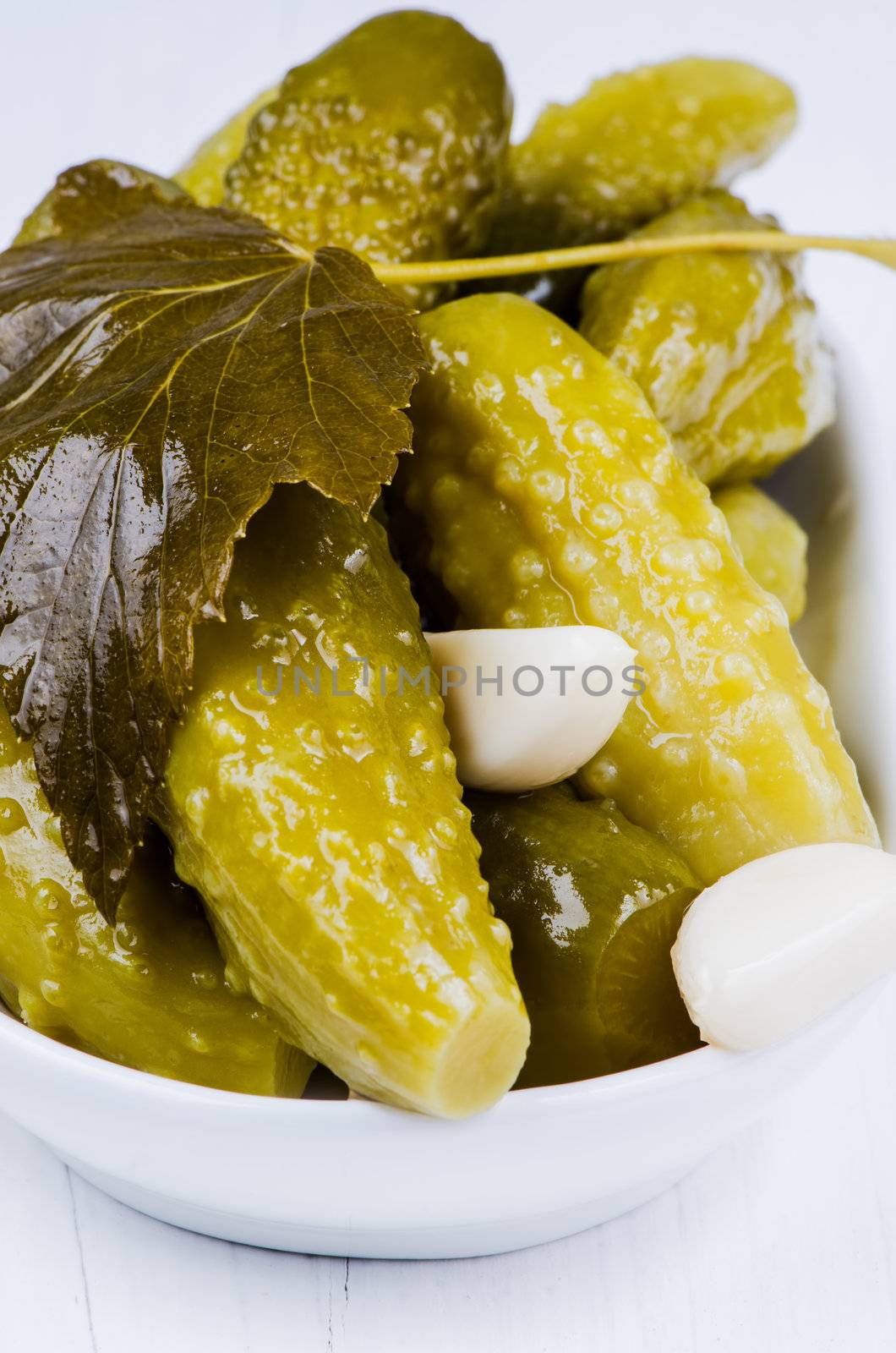 Pickles and garlic in bowl on white wooden table