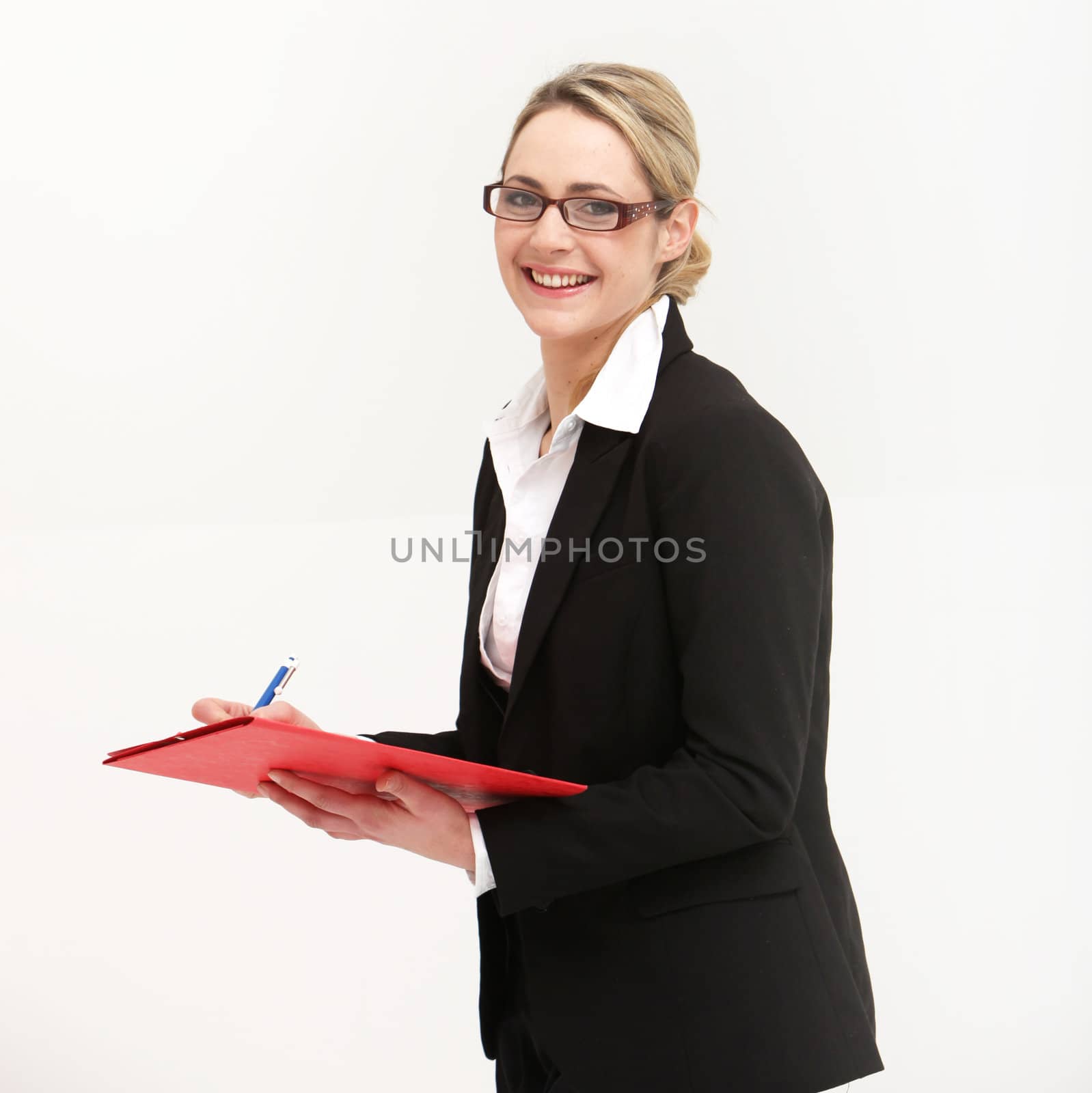 Smiling friendly secretary or assistant wearing glasses writing in a file which she is holding in her hand