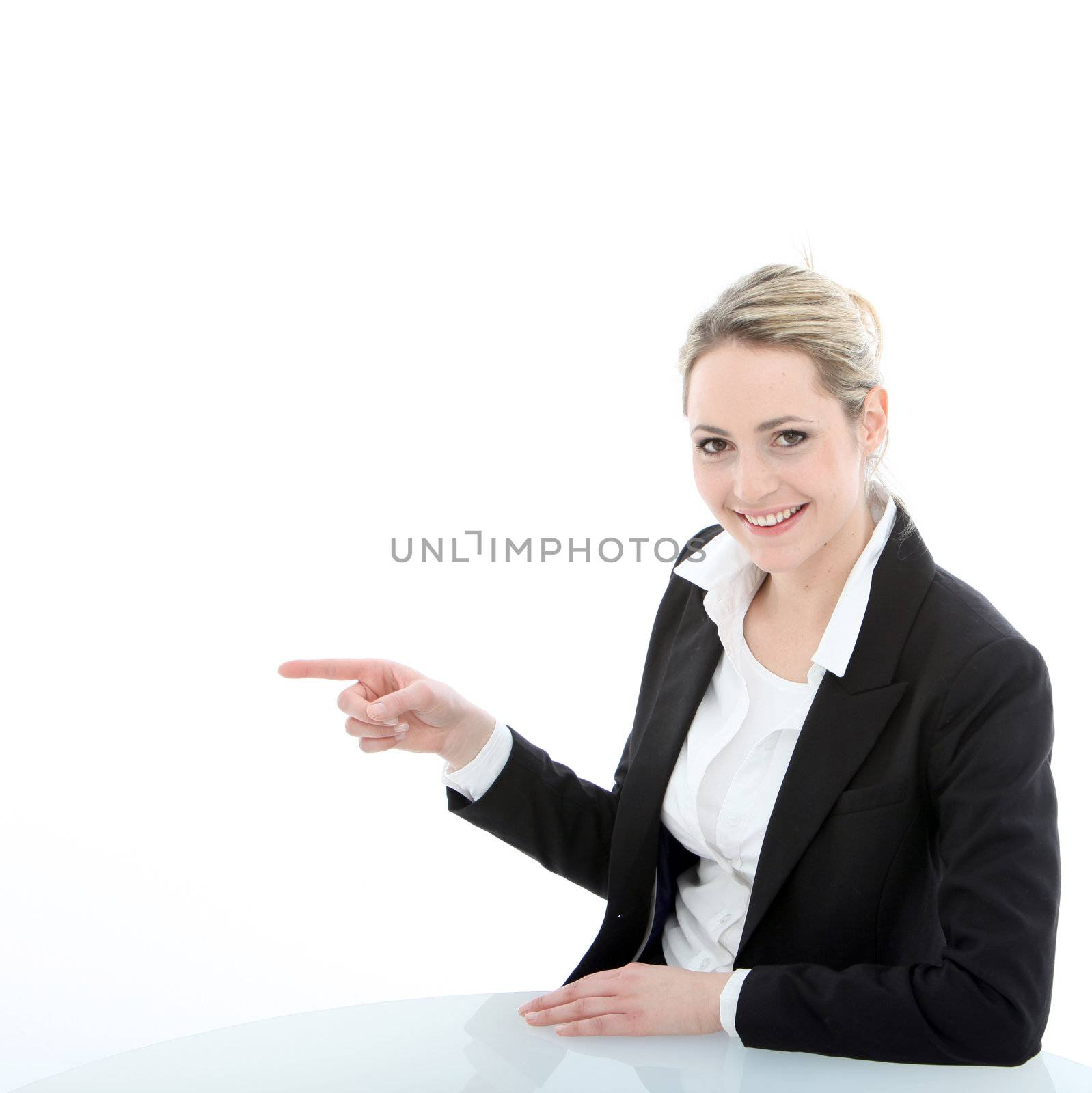 Smiling attractive professional woman seated at a table pointing to her right with her index finger