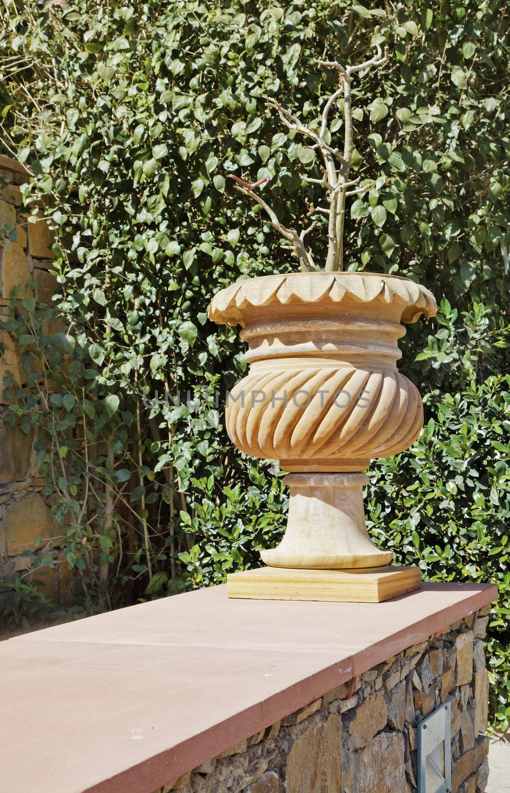 Generic indigenous craft work stone garden flower pot set on the edge of random stone wall with green bushy foliage as a backdrop