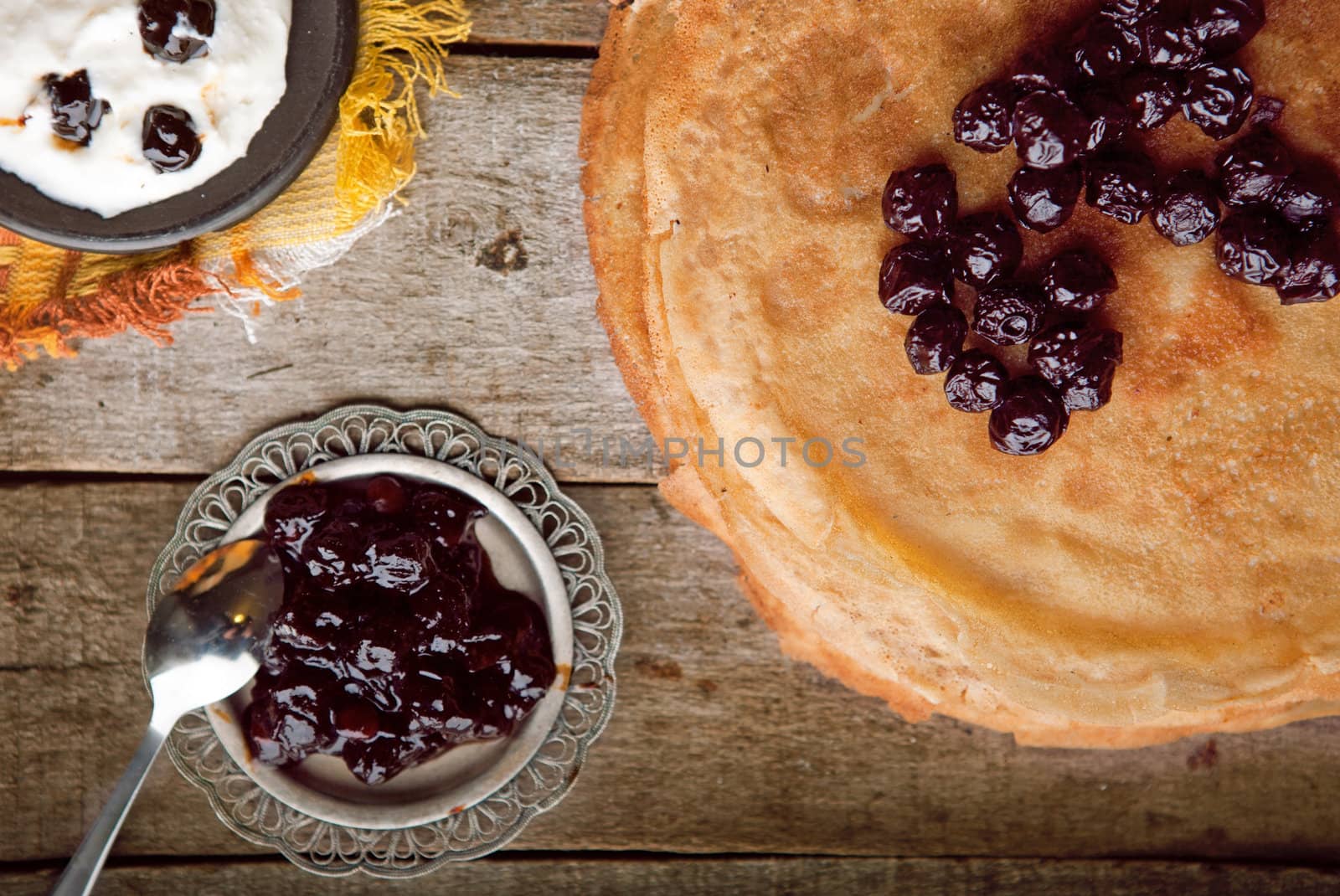 Crepes on the wooden table with cherry with sour cream