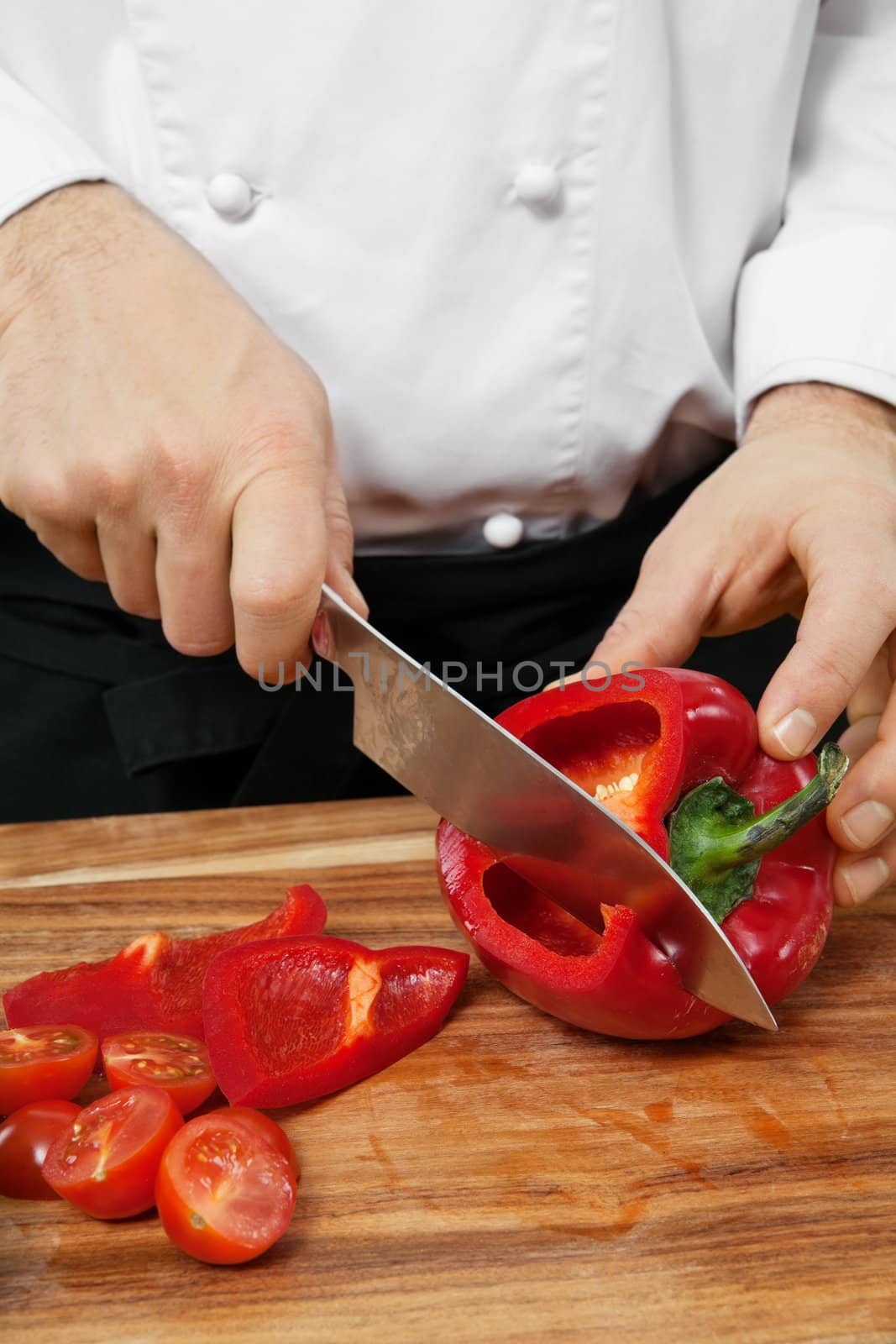 Photo of a chef chopping a red bell pepper on a wooden cutting board.