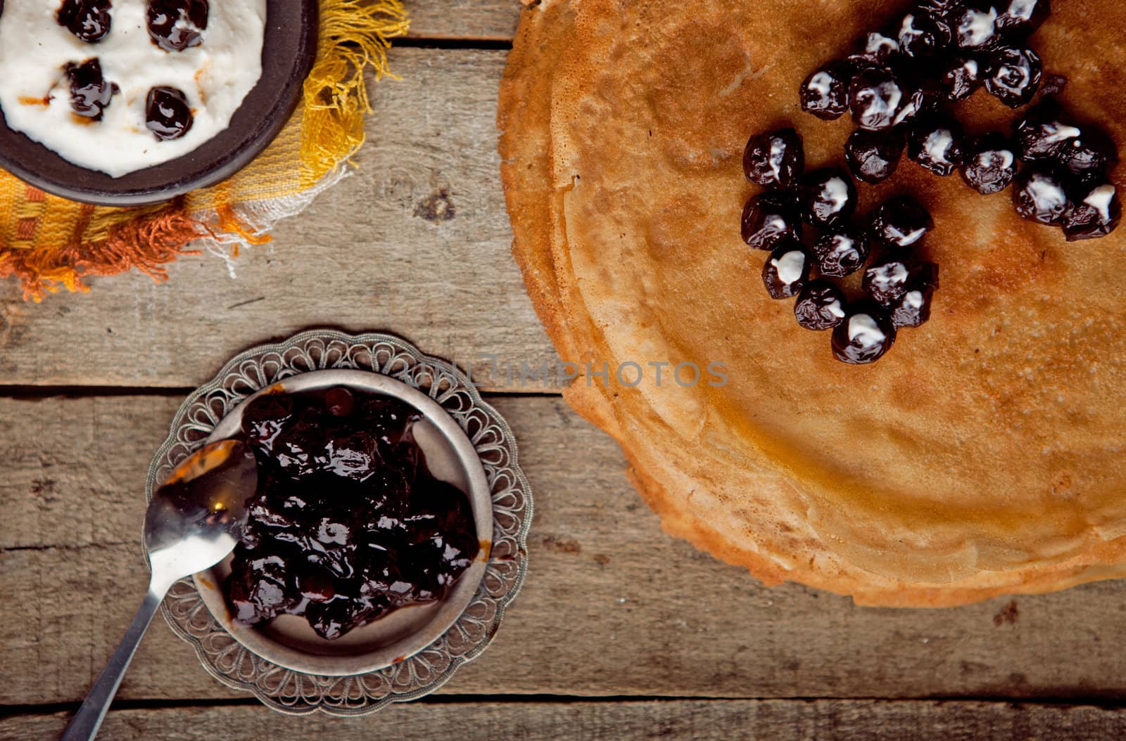 Crepes on the wooden table with cherry with sour cream