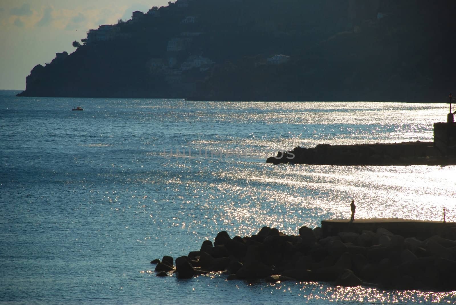 Coast view with a man on a breakwater and a boat in the sea