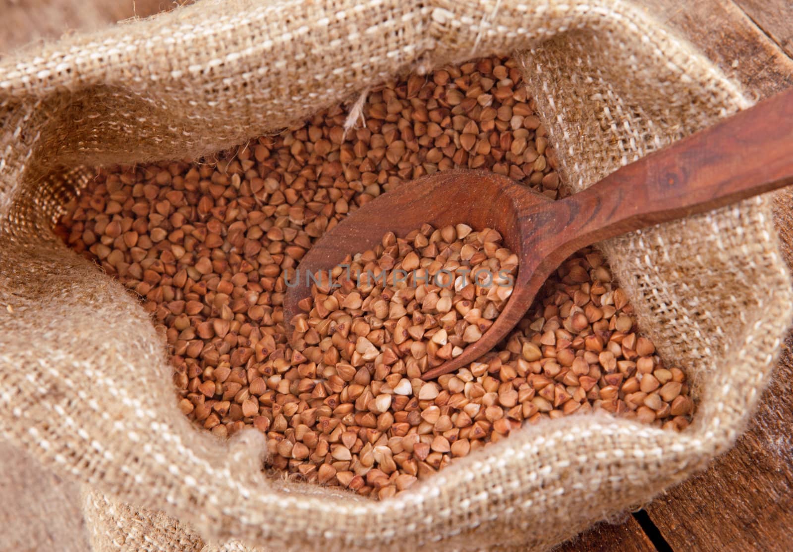 Crude buckwheat on a wooden spoon in the bag