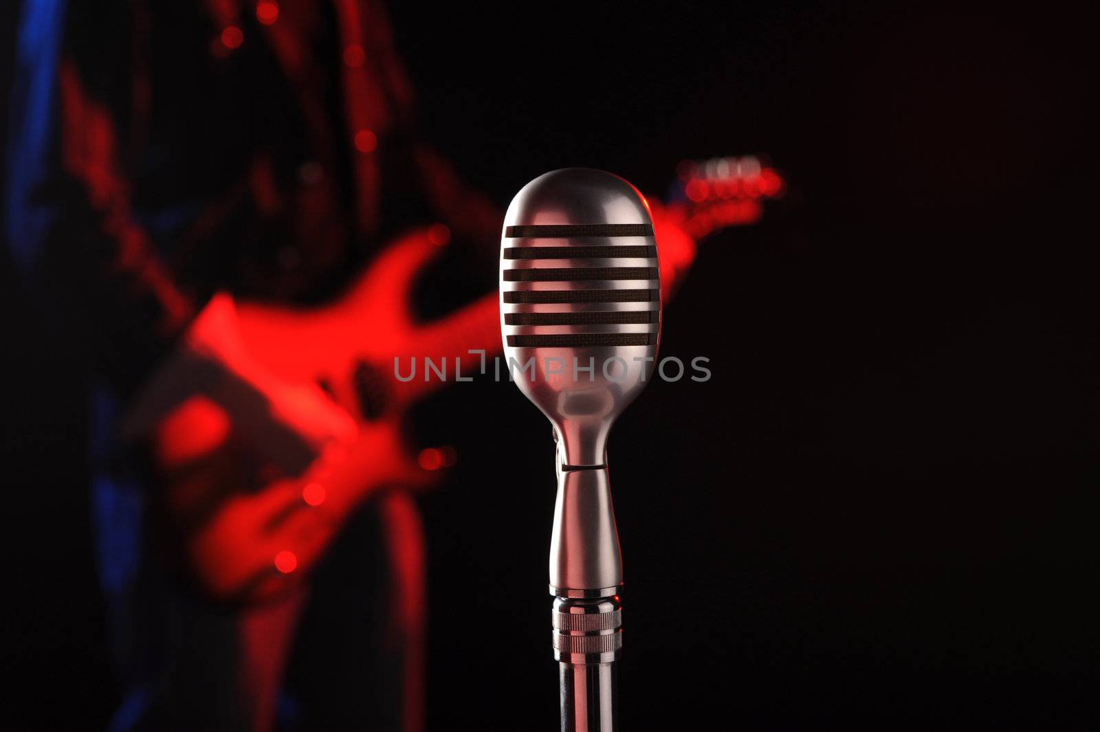 old microphone in the foreground with a guitarist in the background