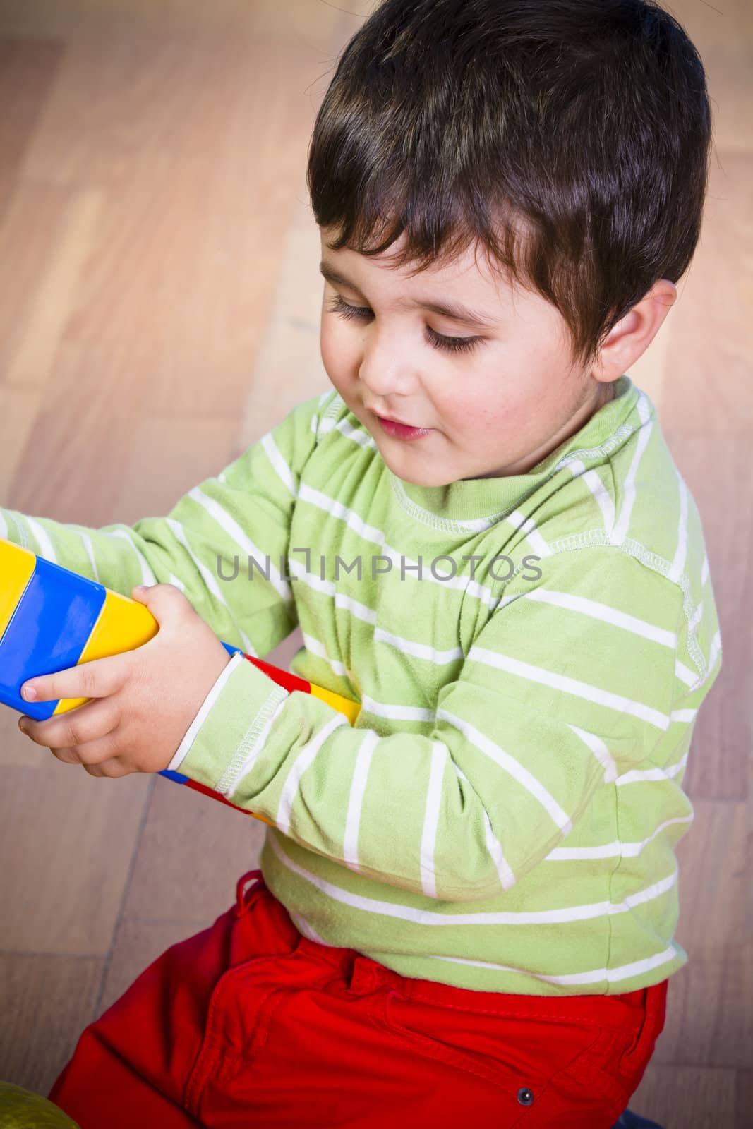 Cute little brunette child is playing with toys while sitting on wooden floor