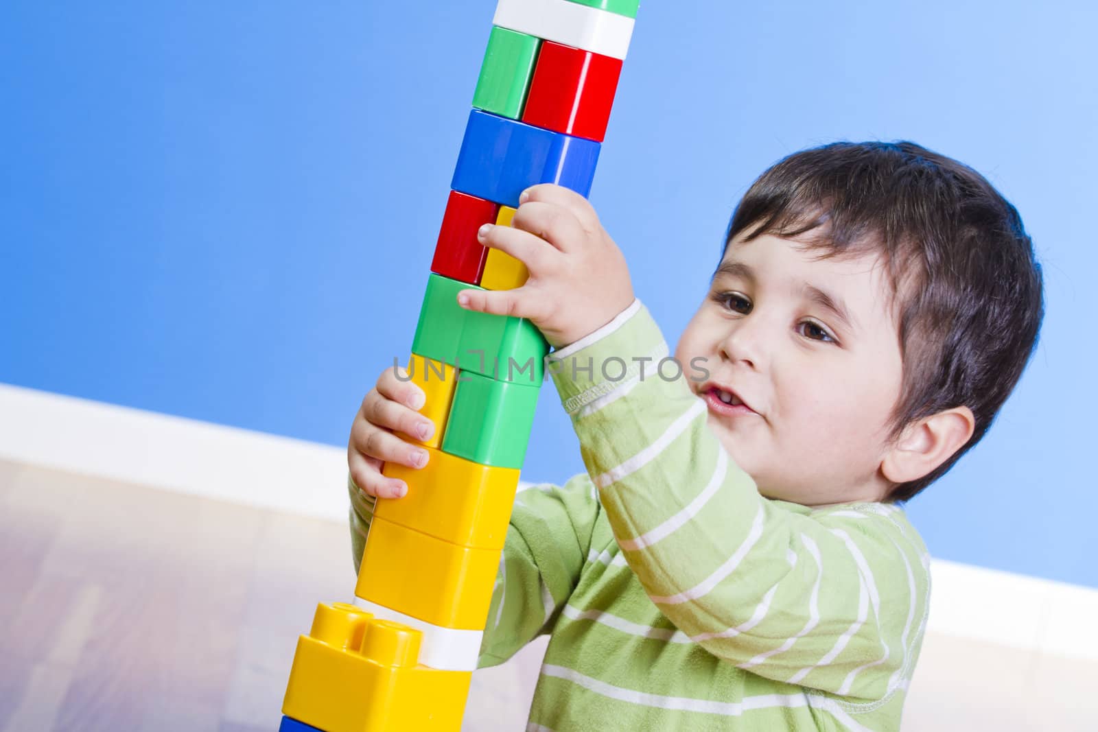 A happy little boy is building a colorful toy block tower