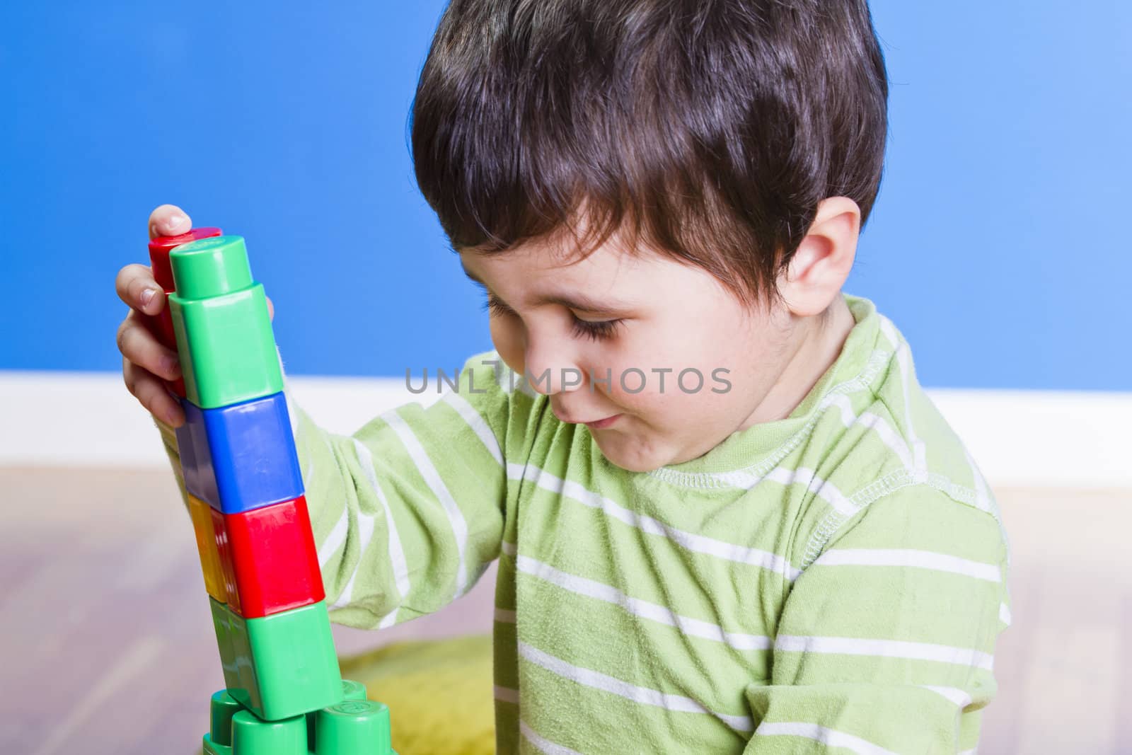 Brunette Baby playing with bright blocks on wooden room