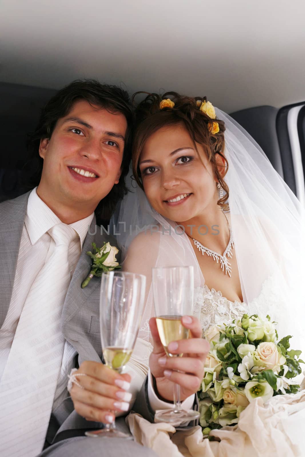 The bride with the groom drinks champagne in the automobile