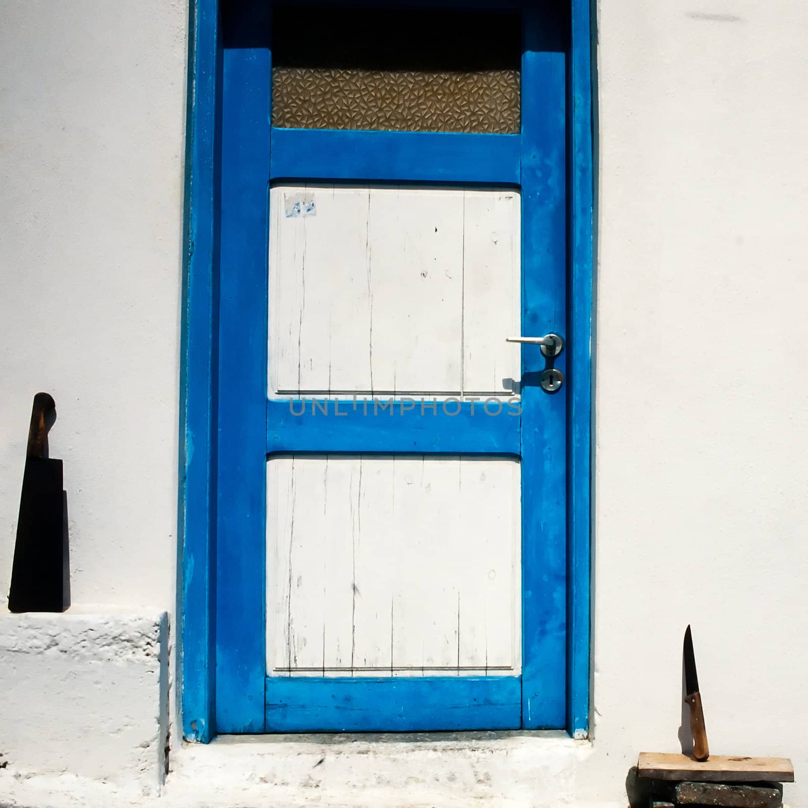 Traditionally painted front door in Greek town with butcher knifes placed to dry in sun.
