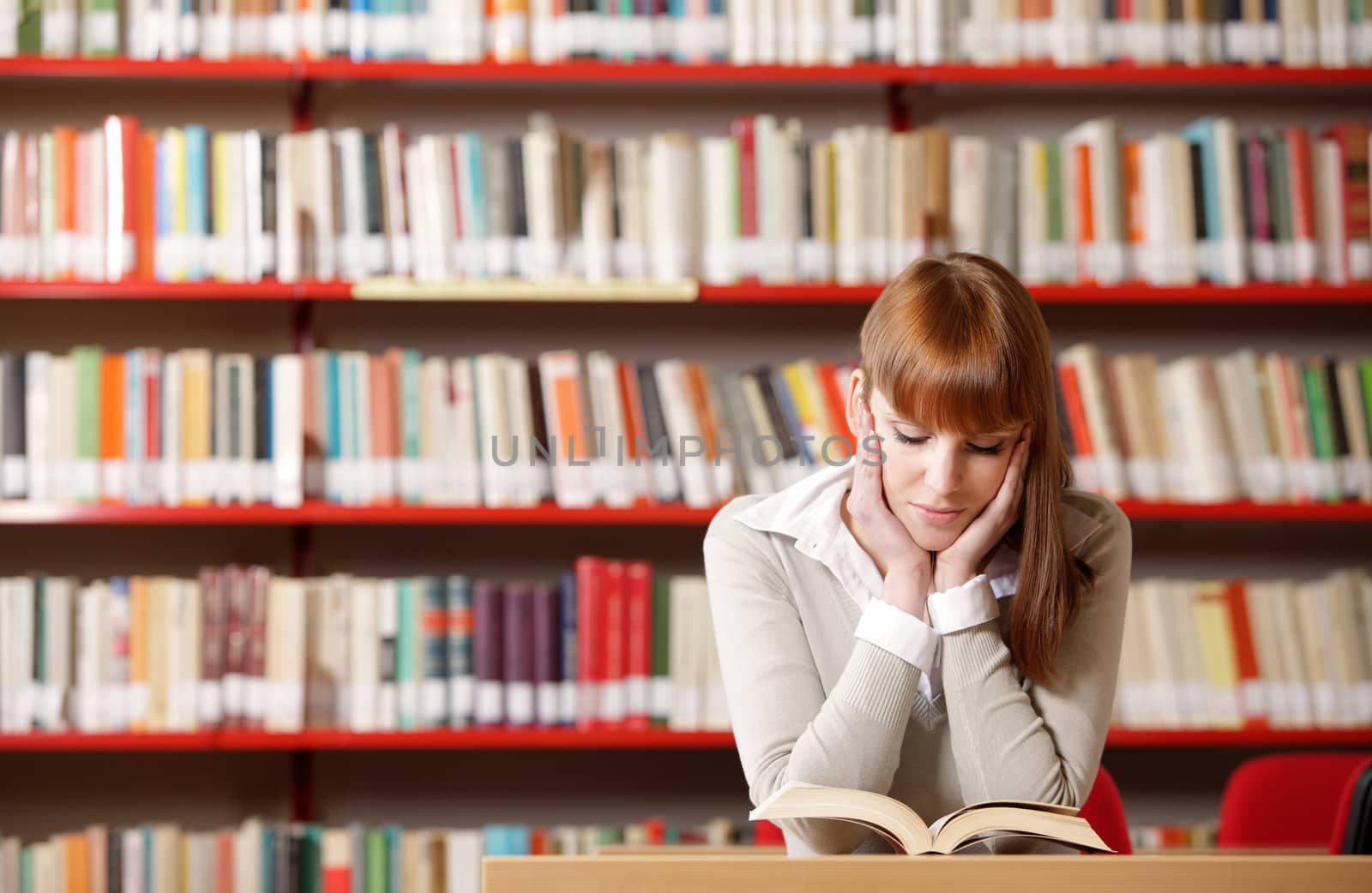 Portrait of a serious young student reading a book in a library 