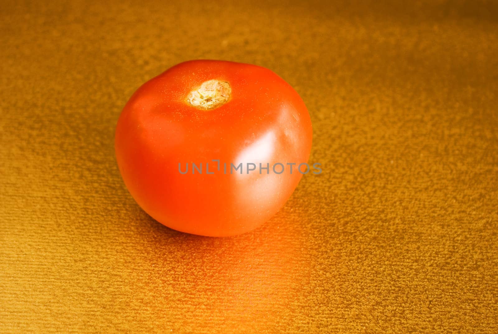 Red tomato on gold background in natural light.