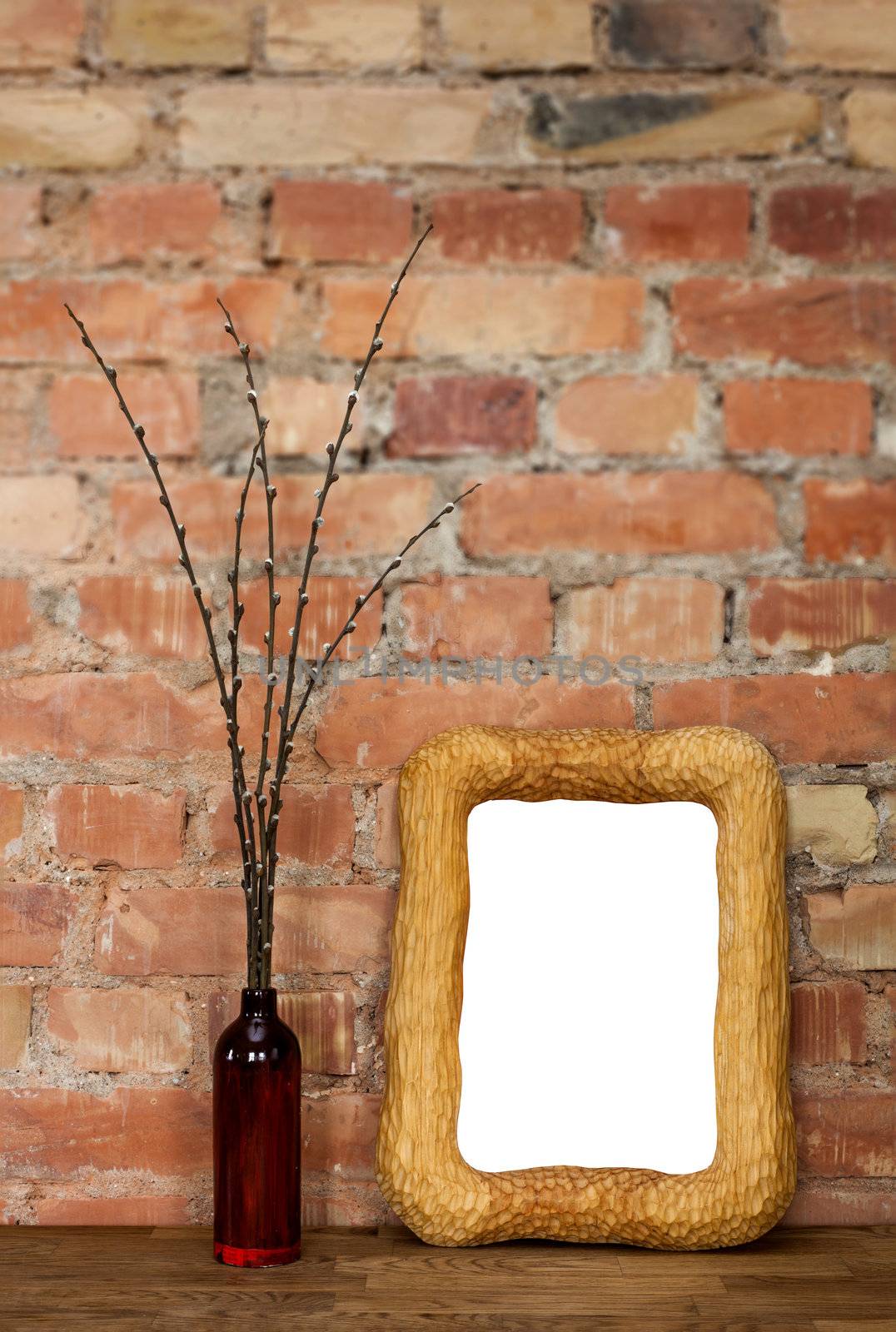 Carved wooden photo frame and brown clay bottle with willow catkins against red brick wall